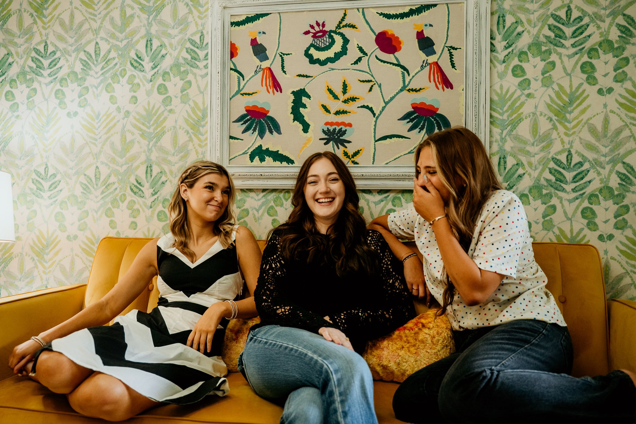 three girls in thrifted clothes sitting on a retro couch laughing uncontrollably