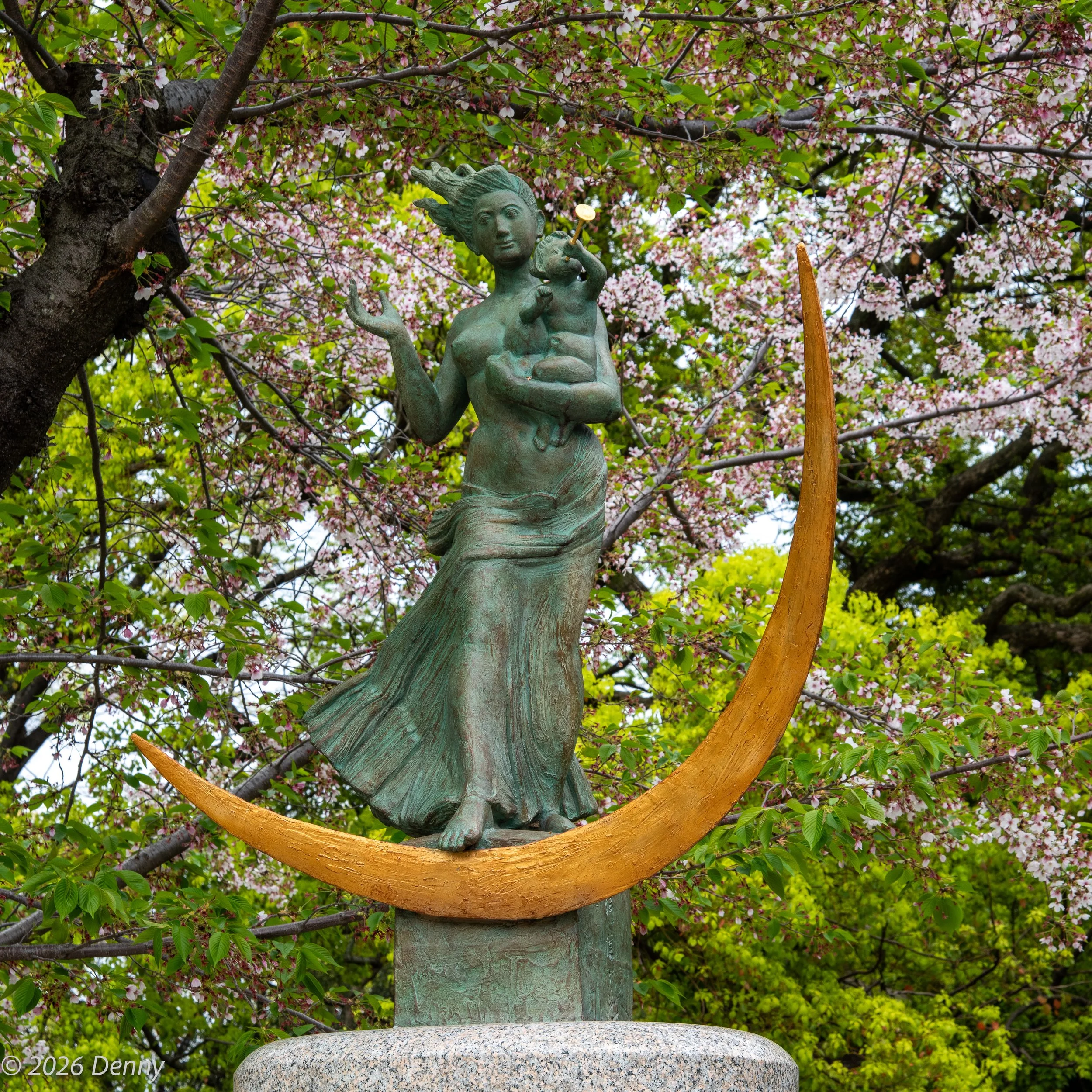 Statue of a woman with her child playing a trumpet standing on a golden crescent moon, Hiroshima Museum gardens, Hiroshima, Japan