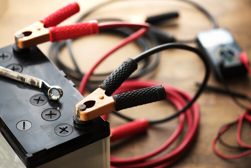 A Car battery with red and black battery Jumper Cables with copper clamps attached to the terminals.