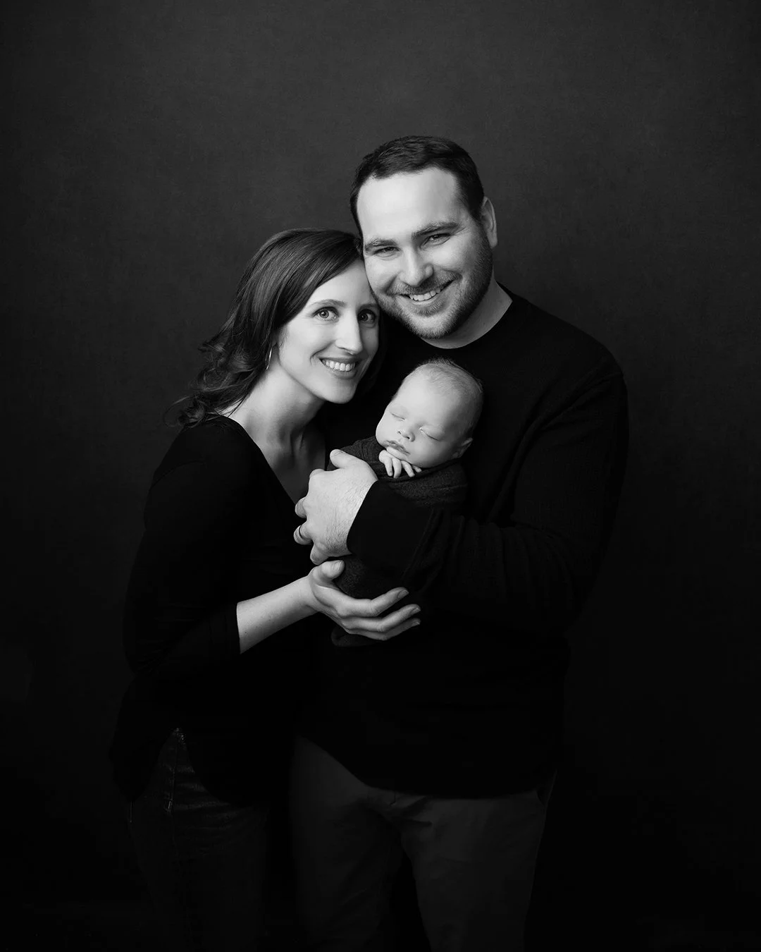 a black and white portrait of a family holding a newborn