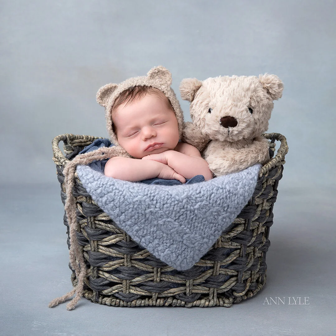 a baby posed in a blue and grey baskets with a teddy bear