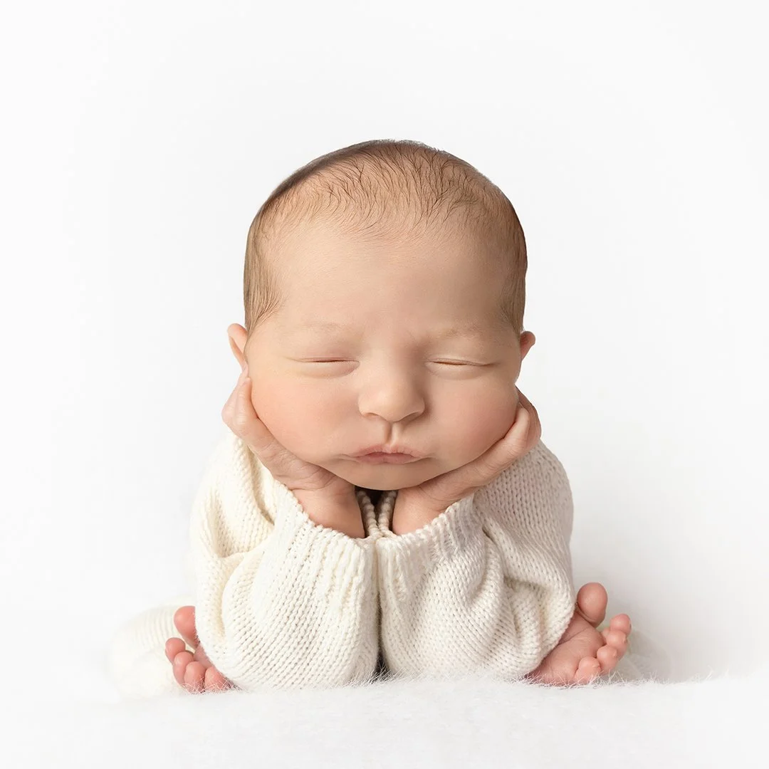 newborn in a white sweater in froggy pose
