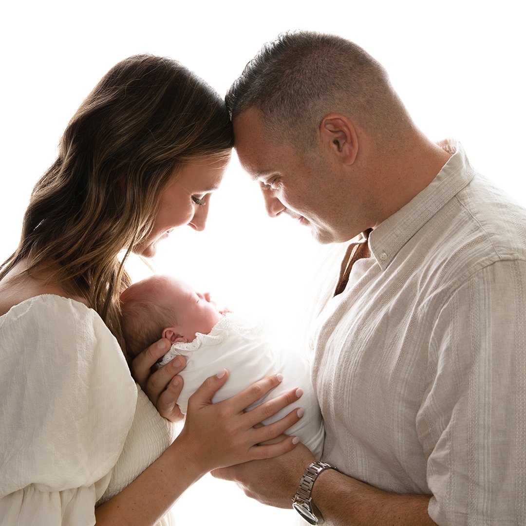 A family holding a newborn baby, all smiling with their foreheads touching.