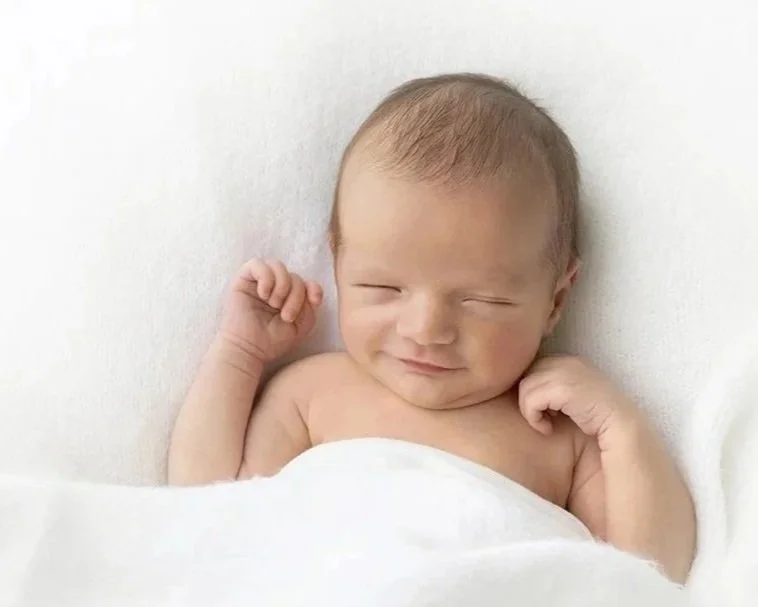 A newborn boy laying in bed with a tiny smile