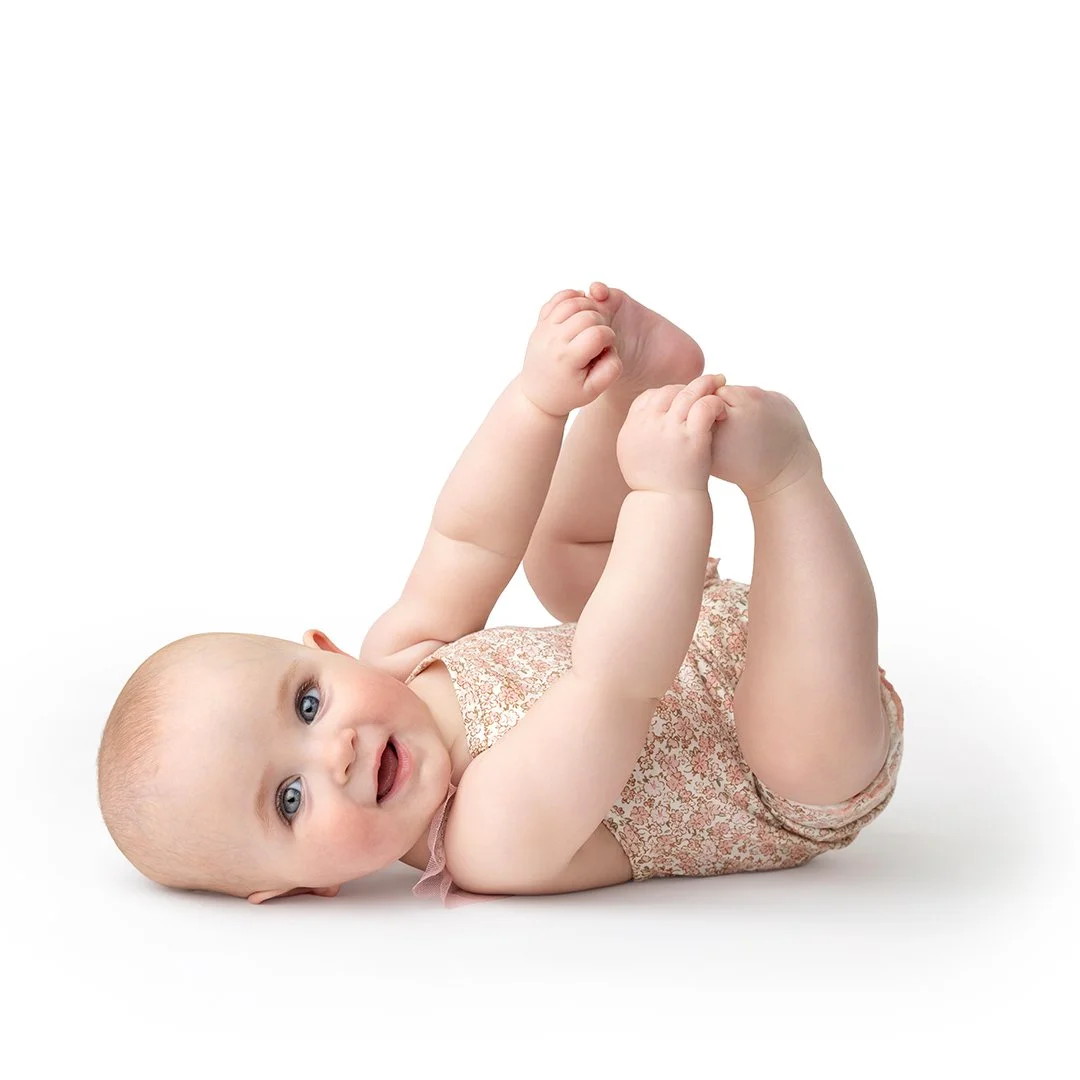 A baby girl grabbing her toes and looking at the camera