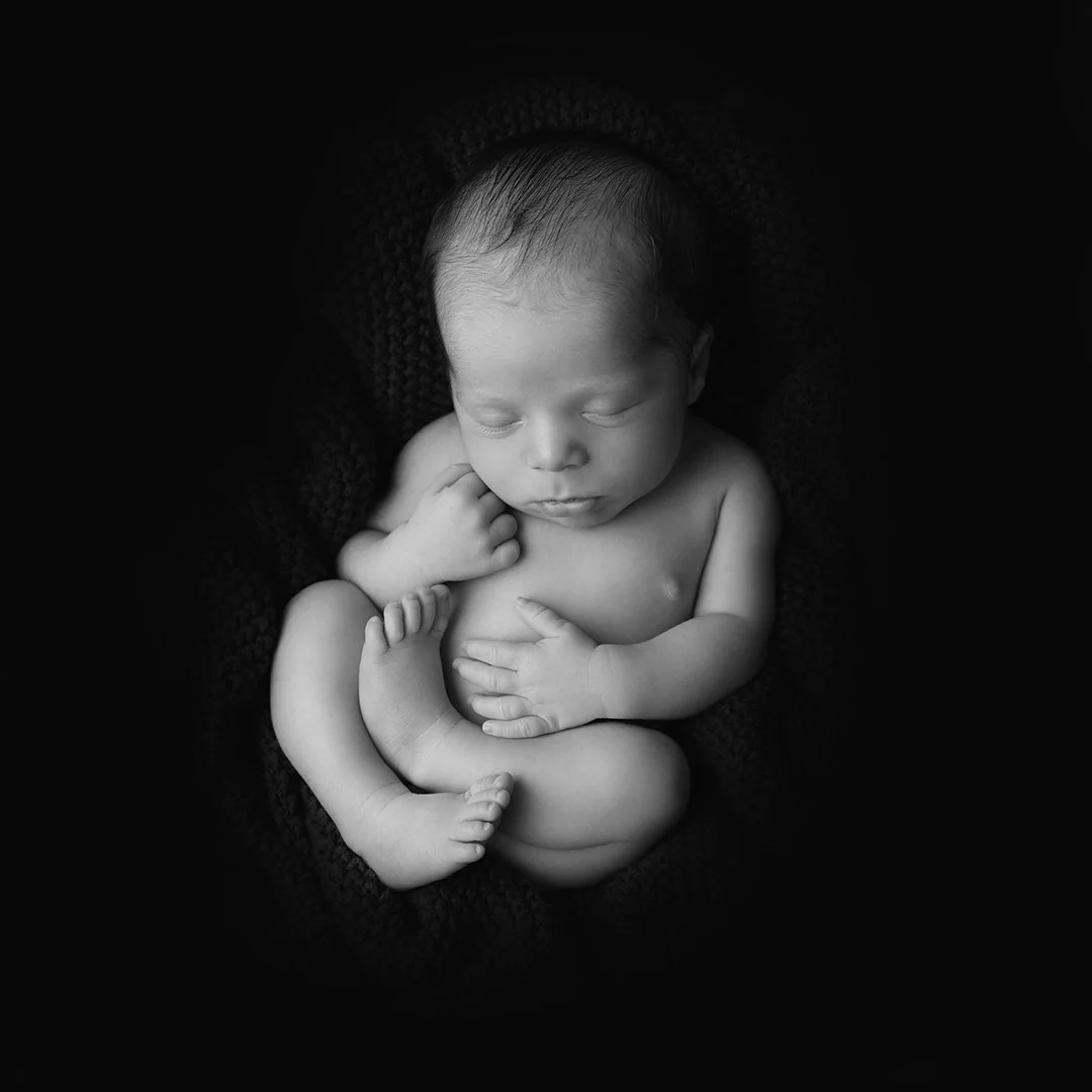 A striking black and white image of a newborn on a black backdrop