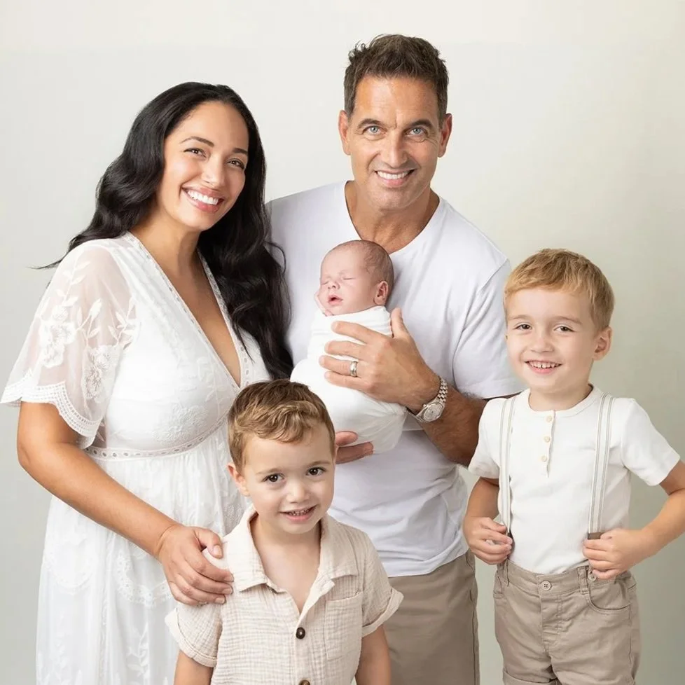 a family dressed in white smiling at the camera with a new baby