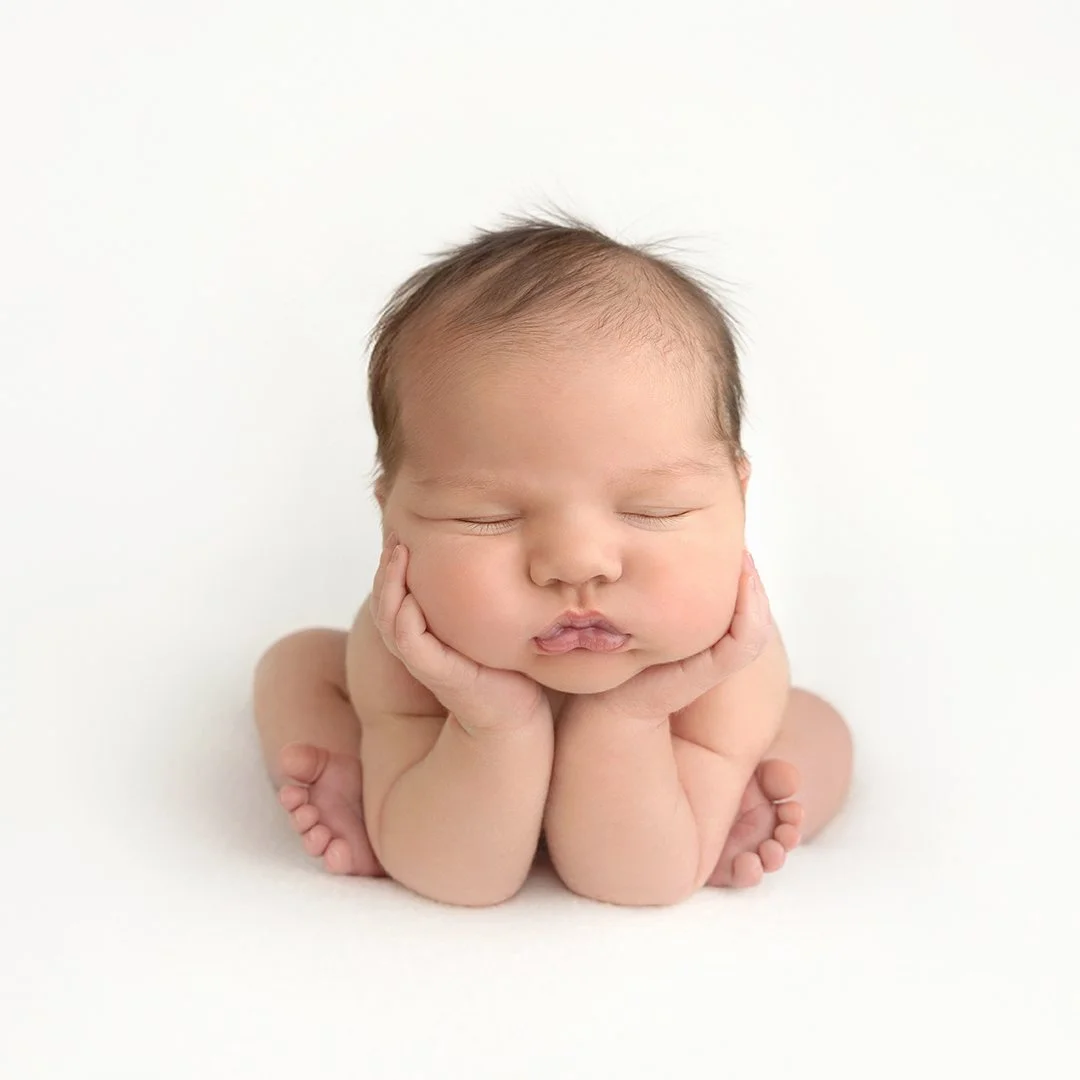 A sleeping baby in a kneeling pose with hands on cheeks, head resting on hands, on a white background.