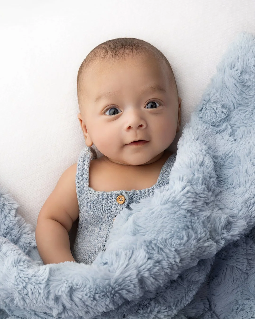 a young baby laying down with a blue blanket.