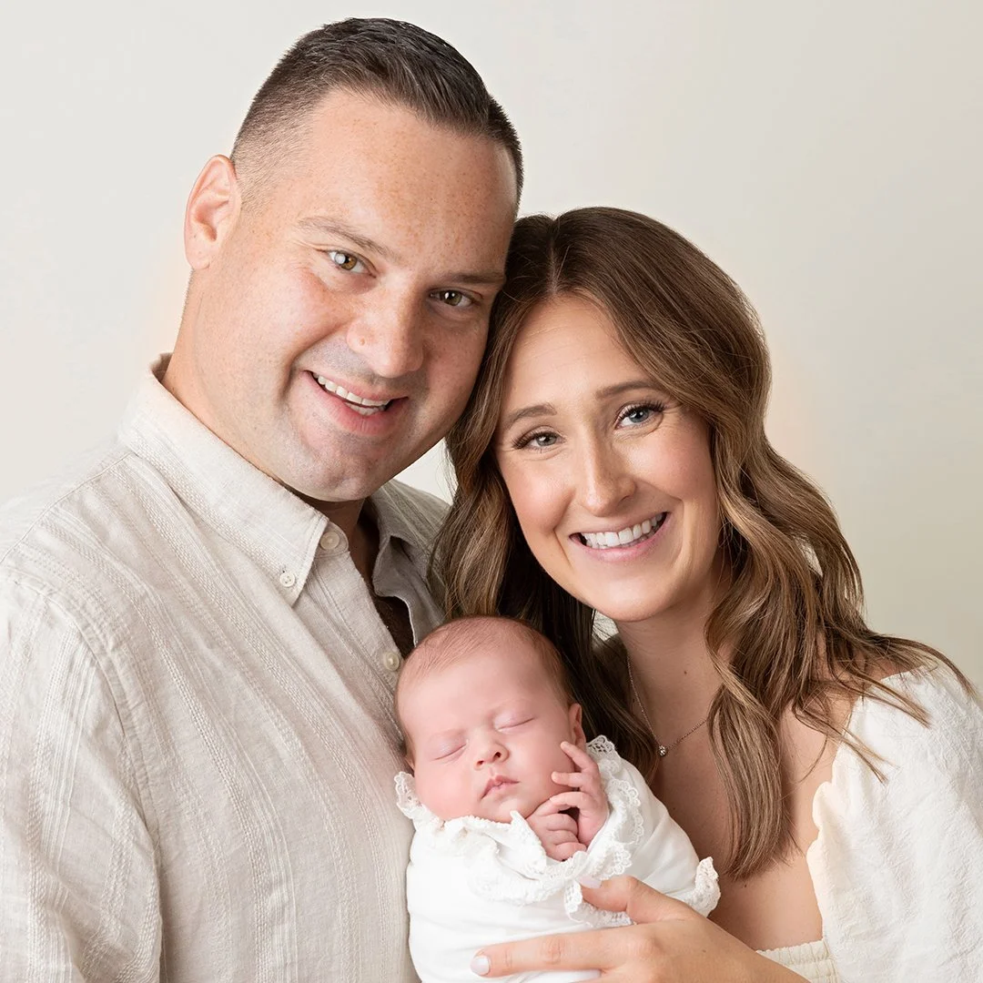 A mother and father holding their newborn on an ivory backdrop