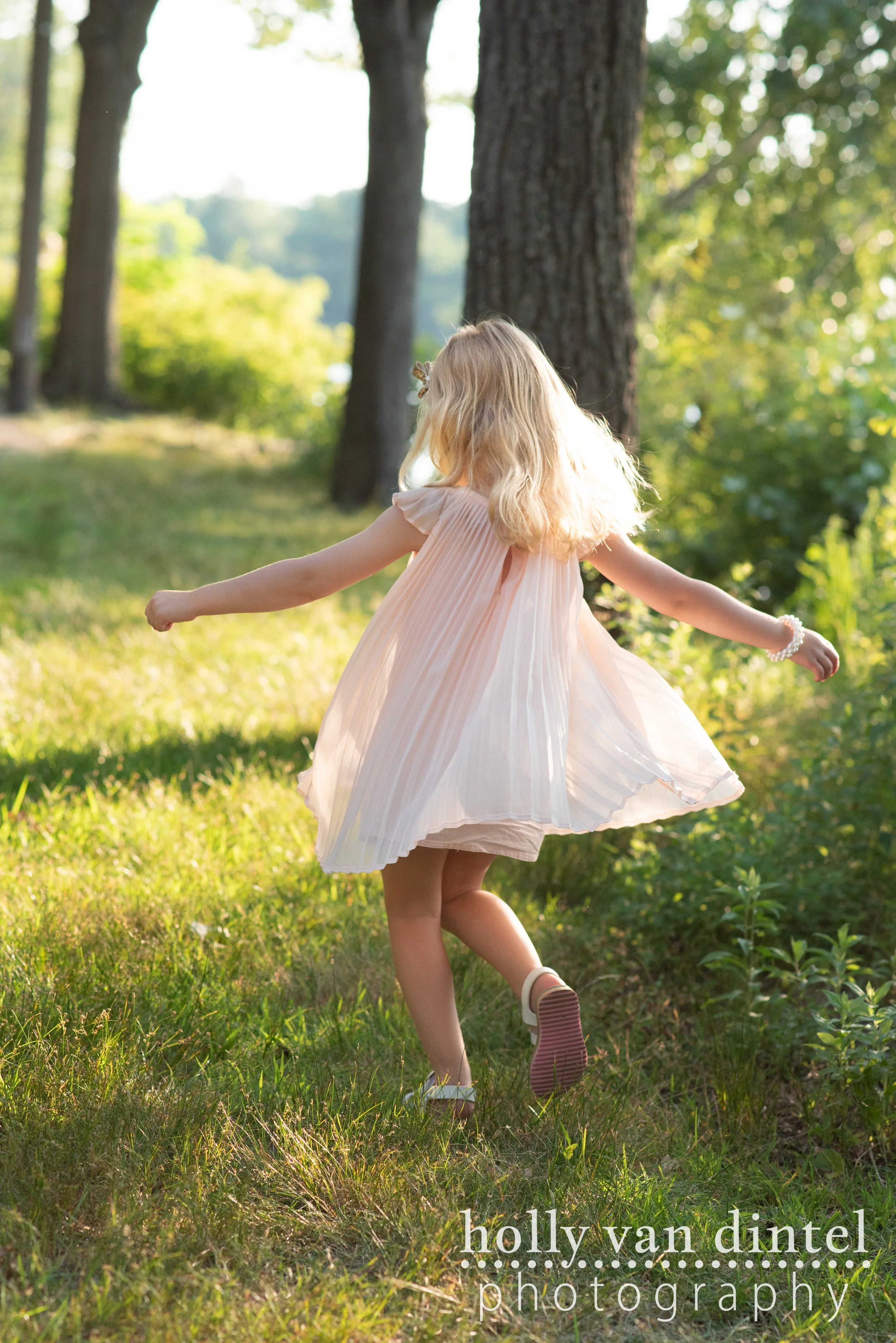 Little girl wearing a pink dress and twirling in the sunshine.