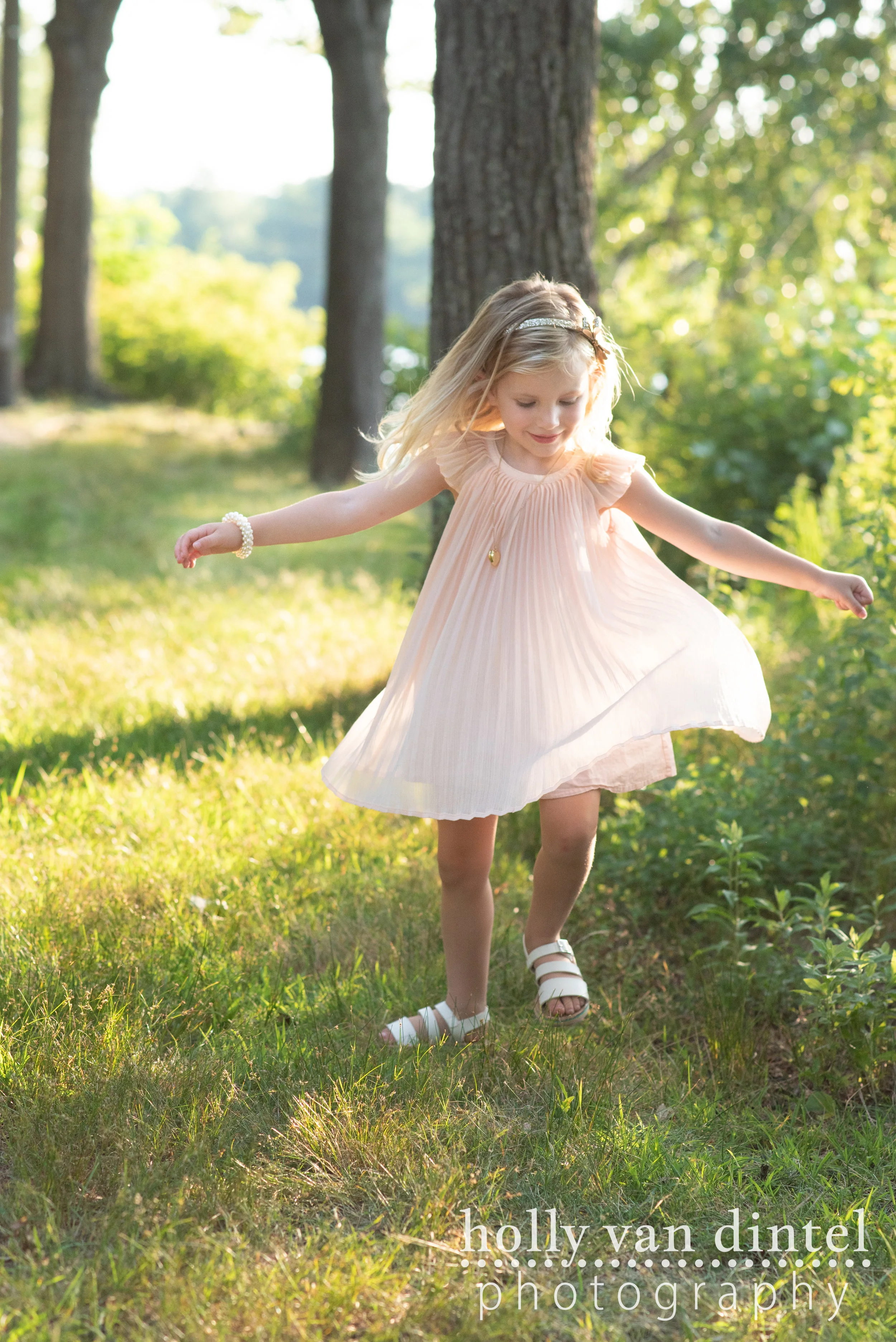 Little girl wearing pink dress and spinning in the sunshine