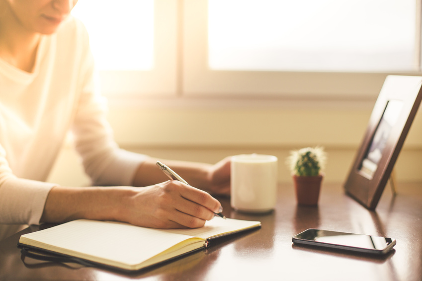 Cropped shot of woman writing and holding coffee cup