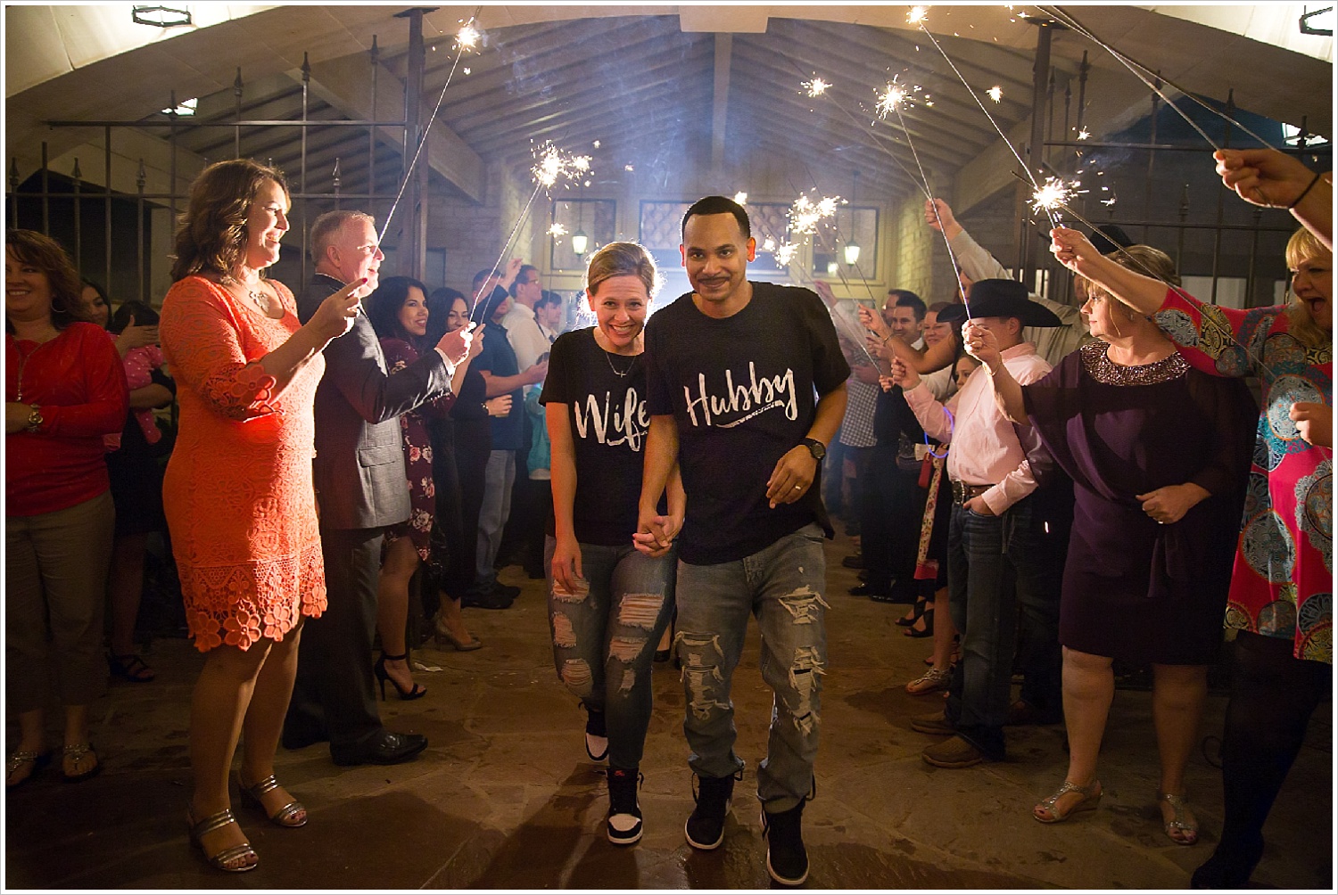 Bride and groom run through sparkler exit wearing matching "Hubby" and "Wifey" shirts at the end of their La Rio Mansion wedding