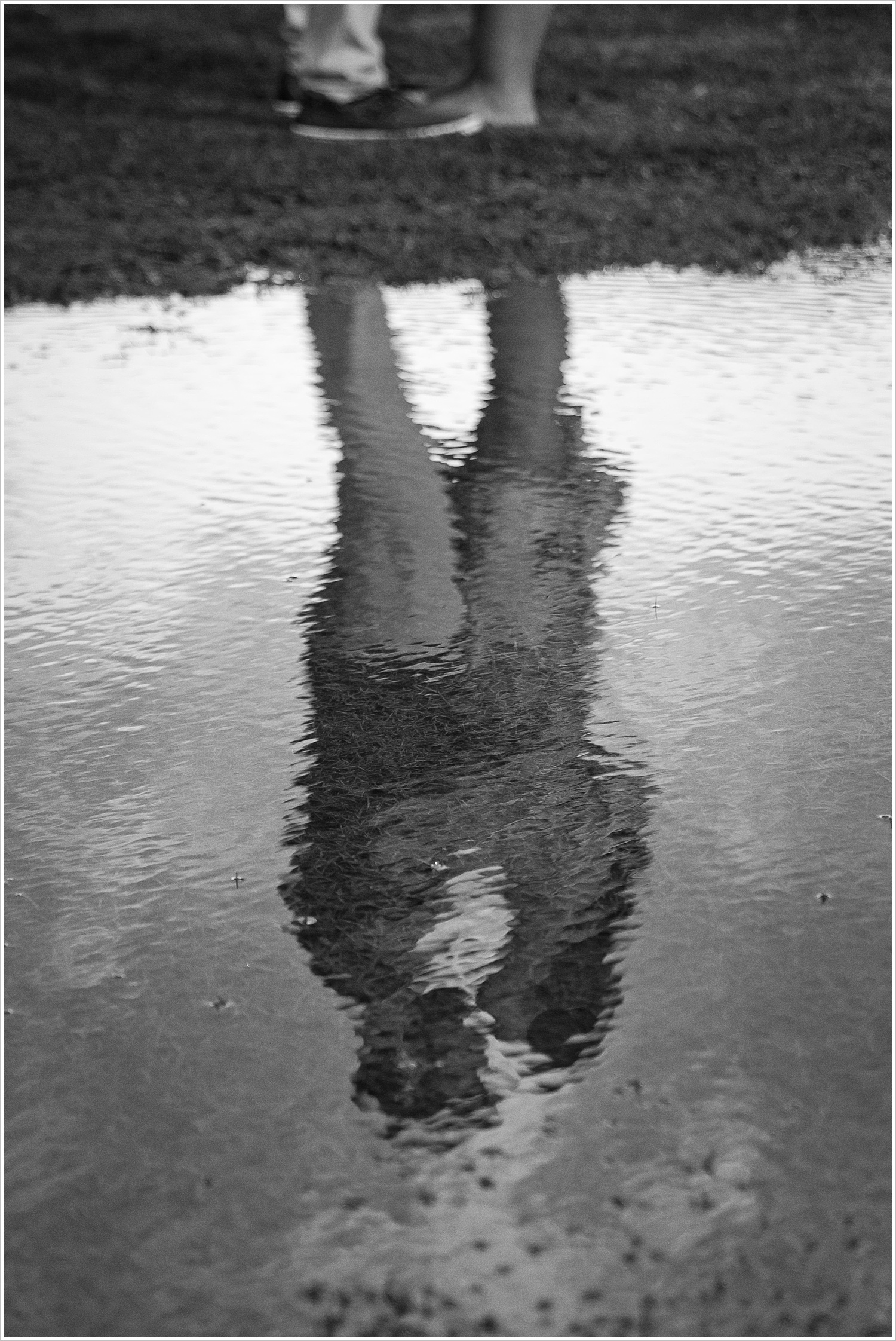 A black and white image of Randell and Fawn's reflection in water Randell & Fawn stand on a bridge in the park where Randell proposed at an engagement photography session in Frisco, Texas by Texas wedding photographers Jason & Melaina Photography, www.jasonandmelaina.com 