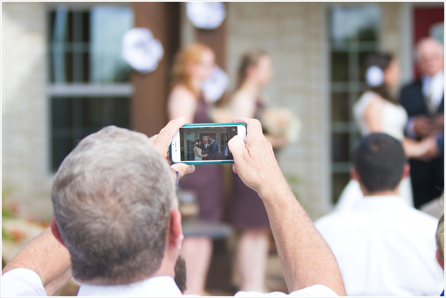 A wedding guest takes a picture of a bride and groom with his cell phone during a wedding ceremony-Should you have an unplugged wedding?, written by Texas Wedding Photographers, Jason & Melaina Photography-www.jasonandmelaina.com 