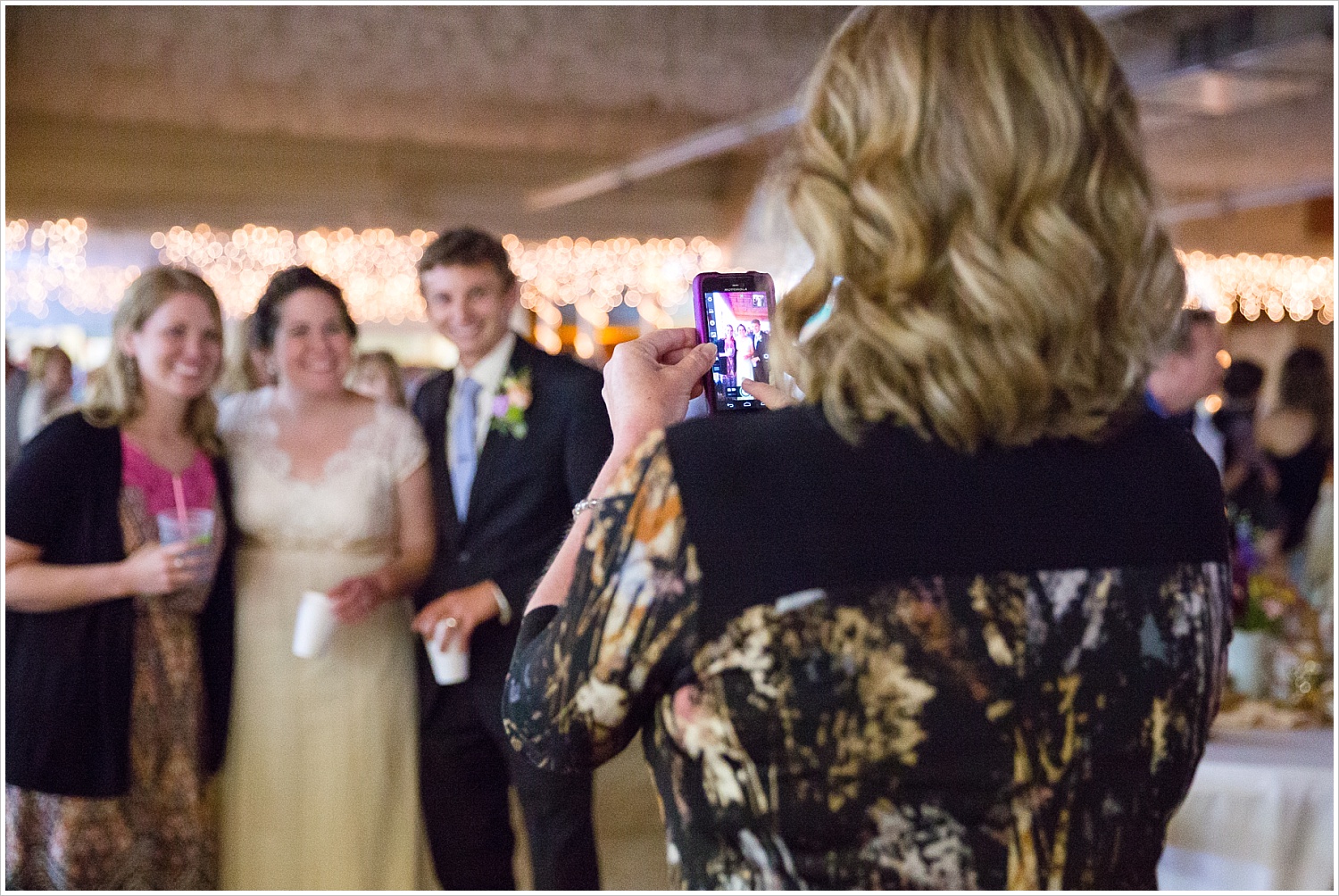 A wedding guest takes a picture of a bride and groom with her cell phone during a wedding reception-Should you have an unplugged wedding?, written by Texas Wedding Photographers, Jason & Melaina Photography-www.jasonandmelaina.com