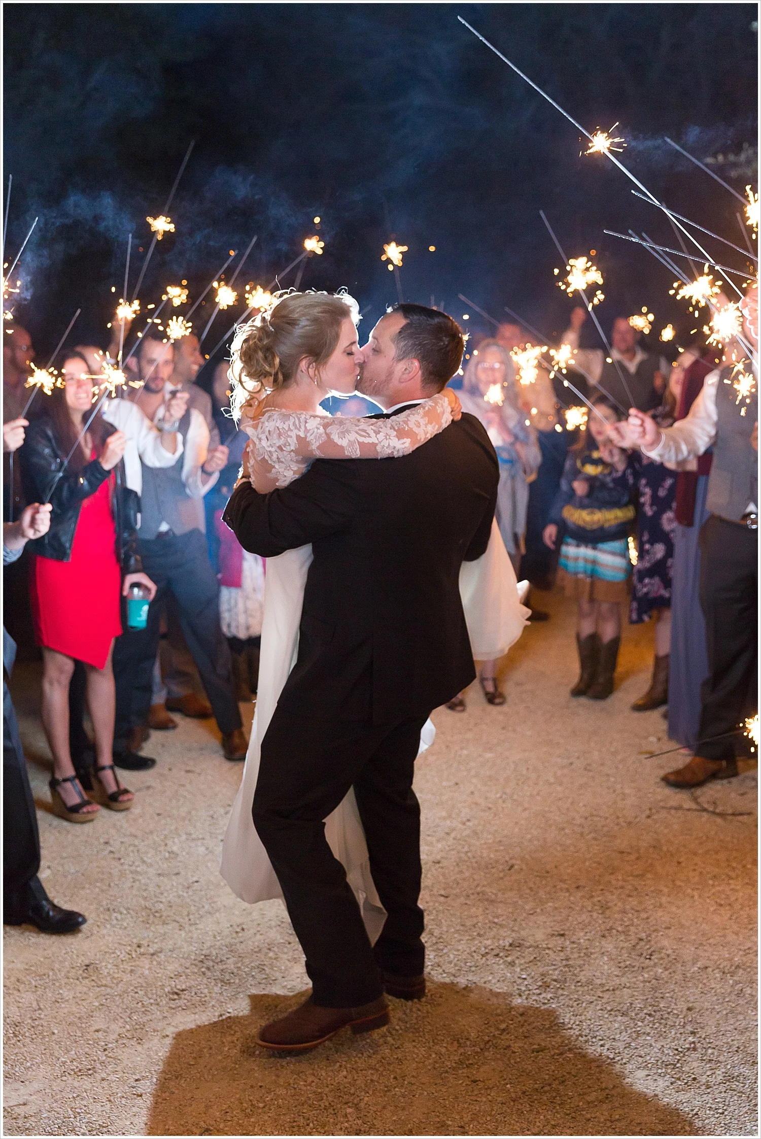 Groom carries his bride and kisses her during their sparkler exit at Bear Creek in Gatesville, Texas - Jason & Melaina Photography - www.jasonandmelaina.com