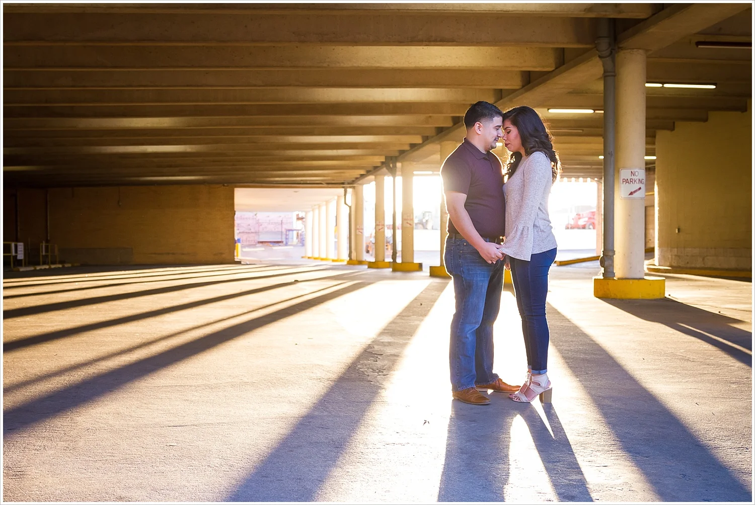 A couple embraces in the sunset in a downtown parking garage during their Waco, Texas engagement photo session - Jason & Melaina Photography - www.jasonandmelaina.com