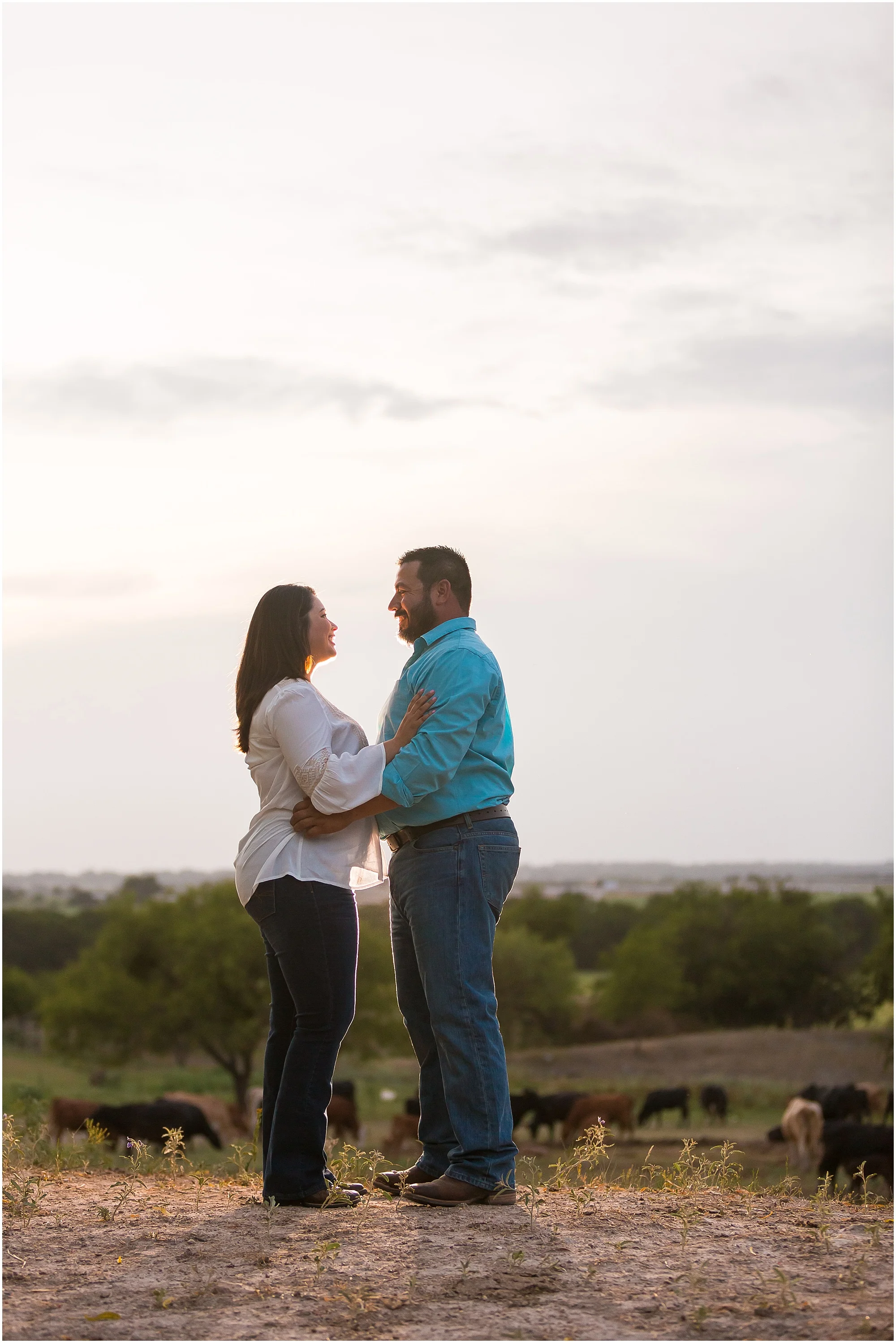 A couple embraces in a field with a Texas sunset behind them during their engagement photos on a family ranch in Dublin, TX - Jason & Melaina Photography - www.jasonandmelaina.com
