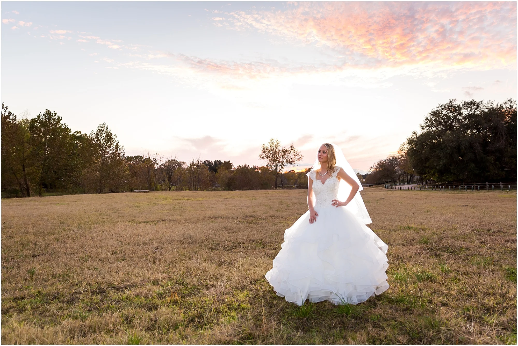 Bride poses in a field with a Texas sunset behind her in Salado, Texas - Jason & Melaina Photography - www.jasonandmelaina.com