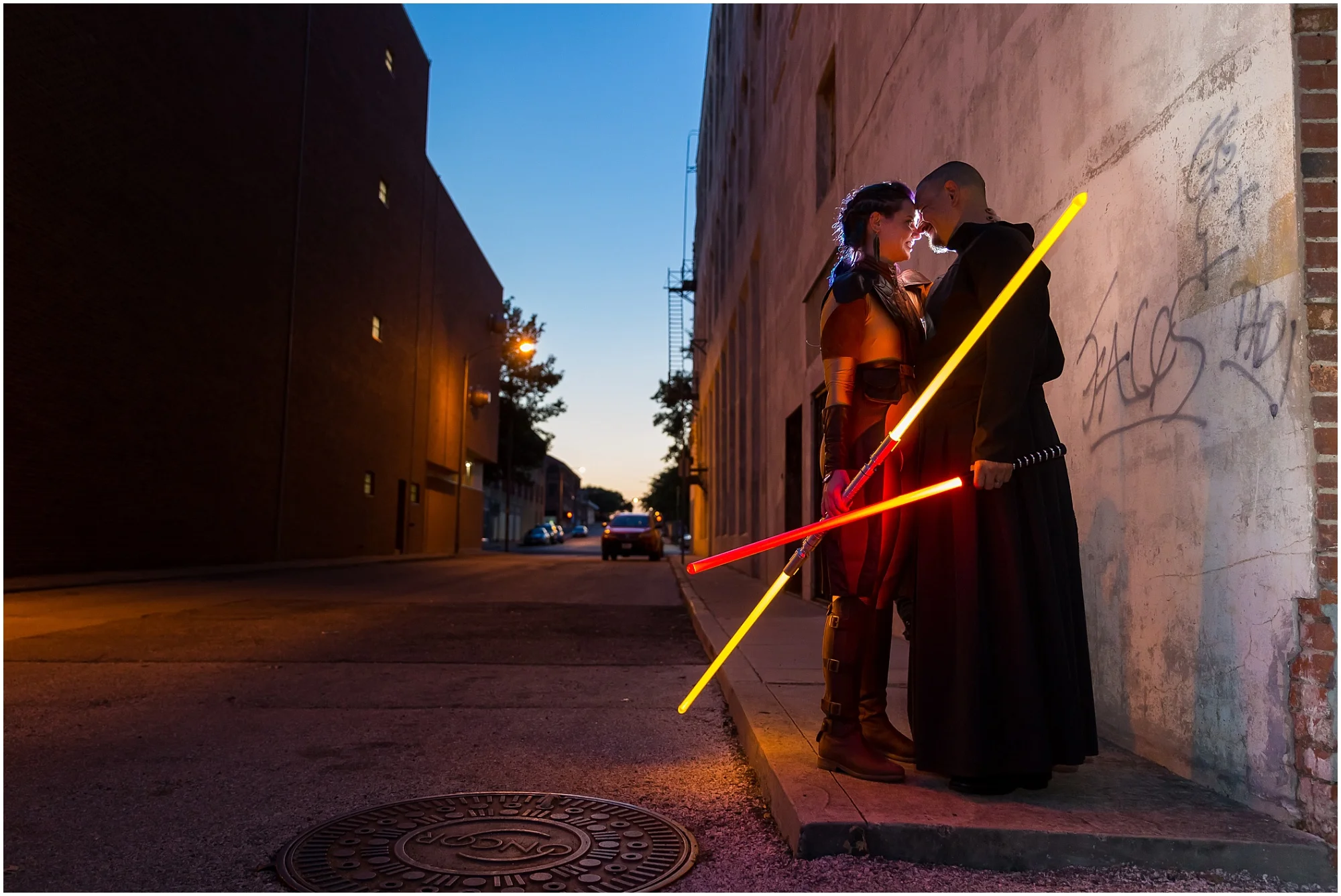 A bride dressed as a Jedi Knight and her groom, dressed as a Sith Lord, embrace holding lightsabers down a darkened alley in downtown Waco, Texas - Jason & Melaina Photography - www.jasonandmelaina.com