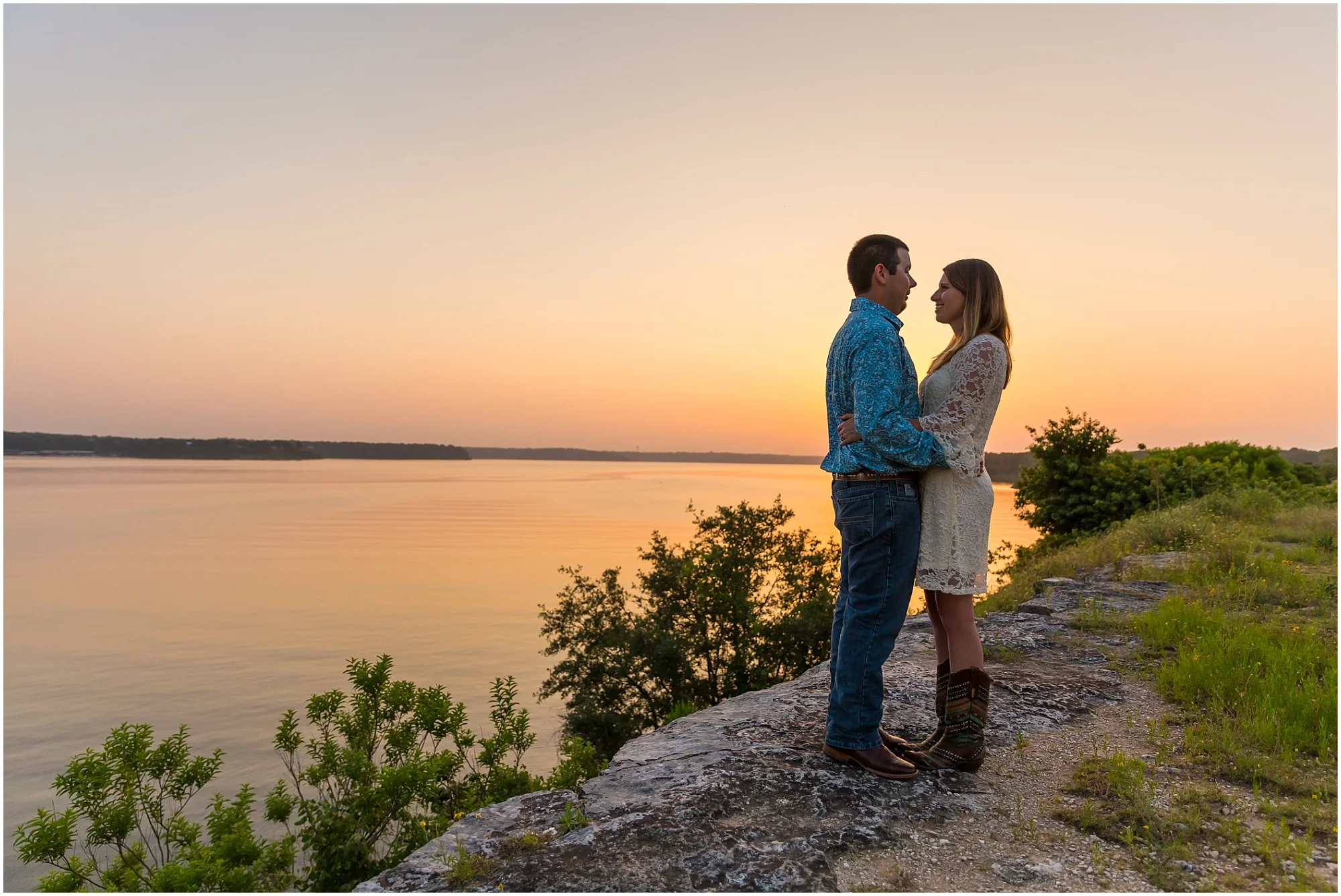 A couple embraces at the Belton Lake Dam while the sun sets over the lake behind them - Jason & Melaina Photography - www.jasonandmelaina.com