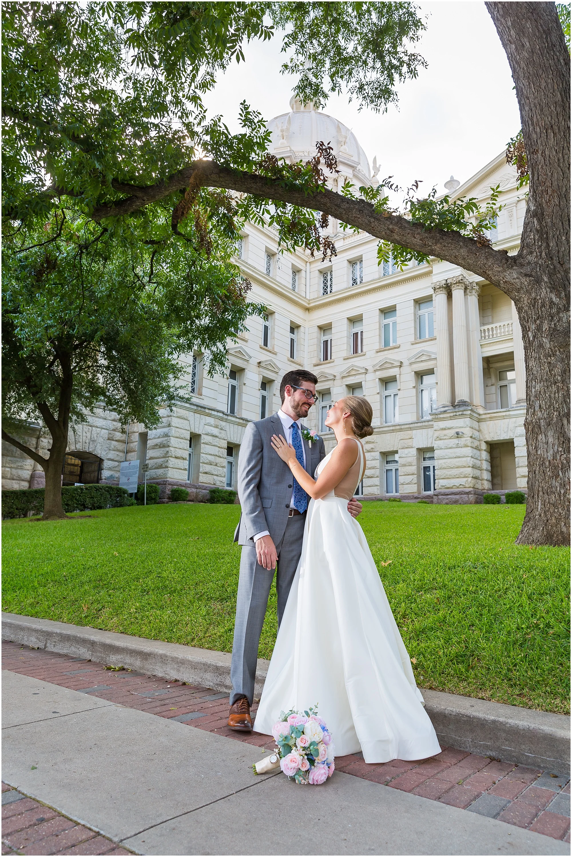 A bride and groom hold one another outside the McLennan County Courthouse in Waco, Texas | Jason & Melaina Photography