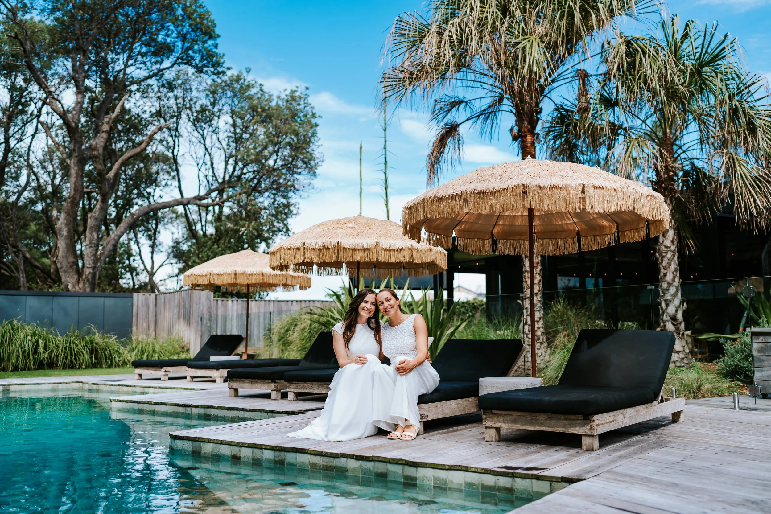 Same sex wedding brides sitting together next to pool