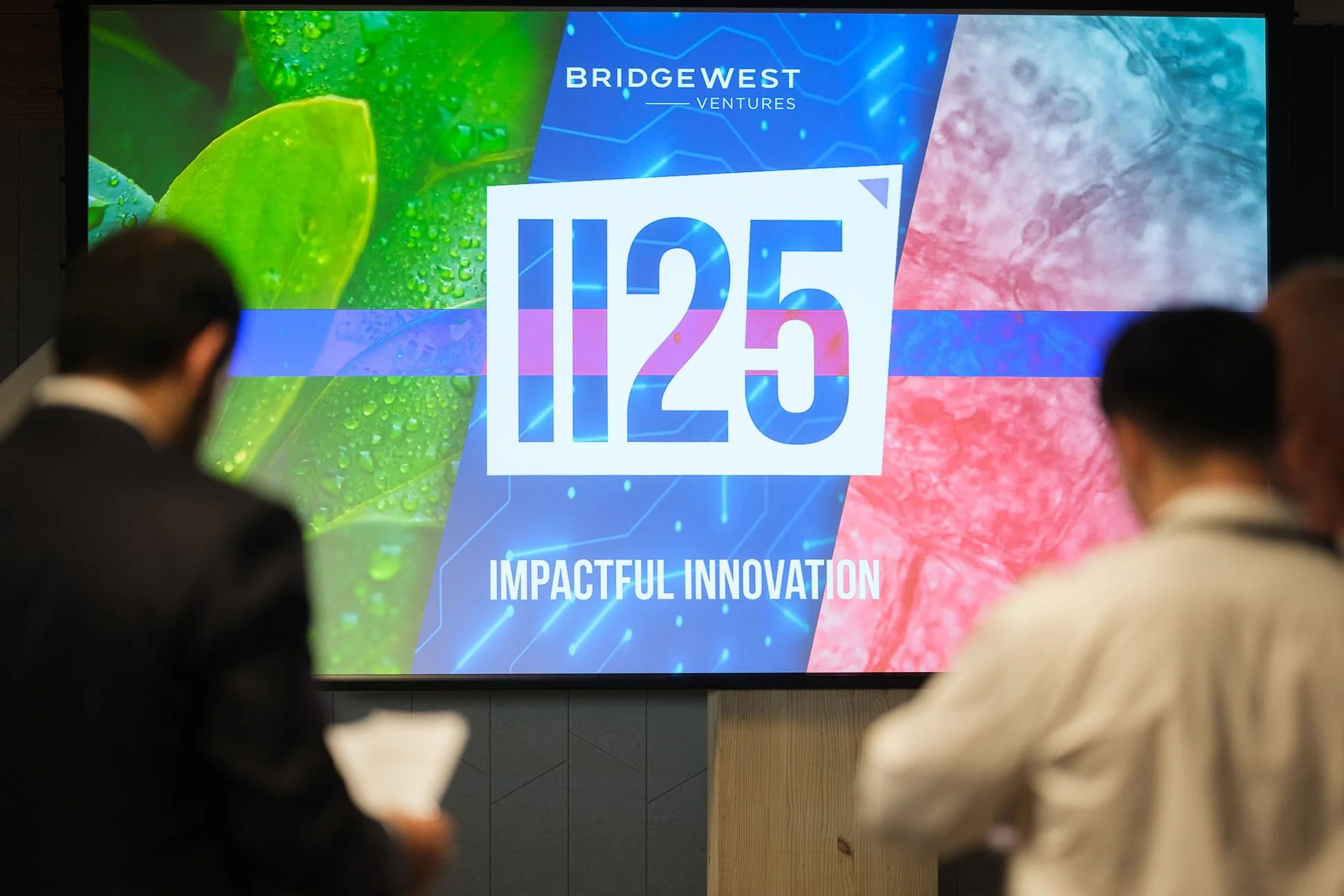 Photo of figures standing in front of a projector screen with the conference brand projected onto it.
