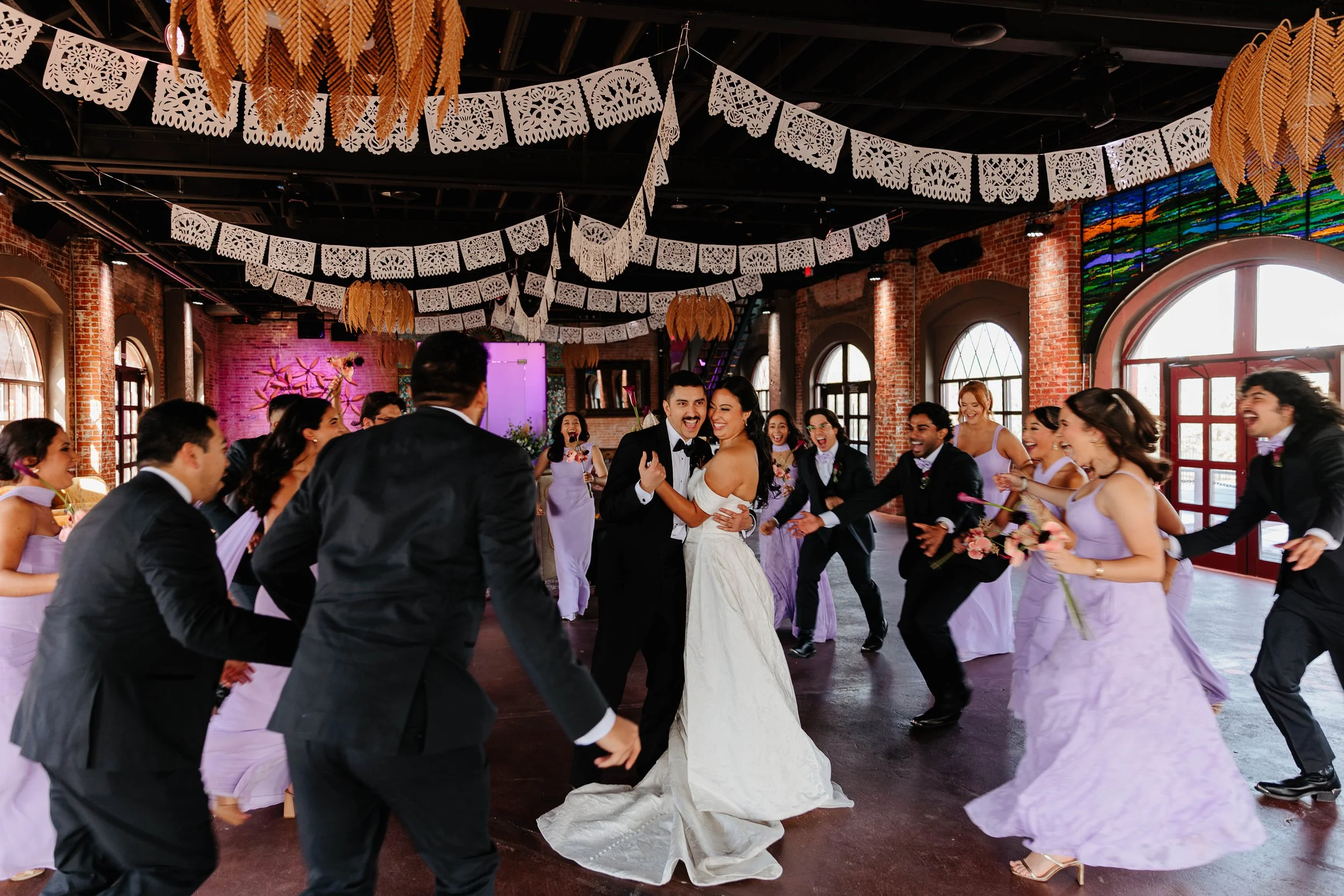 Joyful bride and groom photographed at St Rogers Depot in El Paso receives a big group hug from their bridesmaids and groomsmen