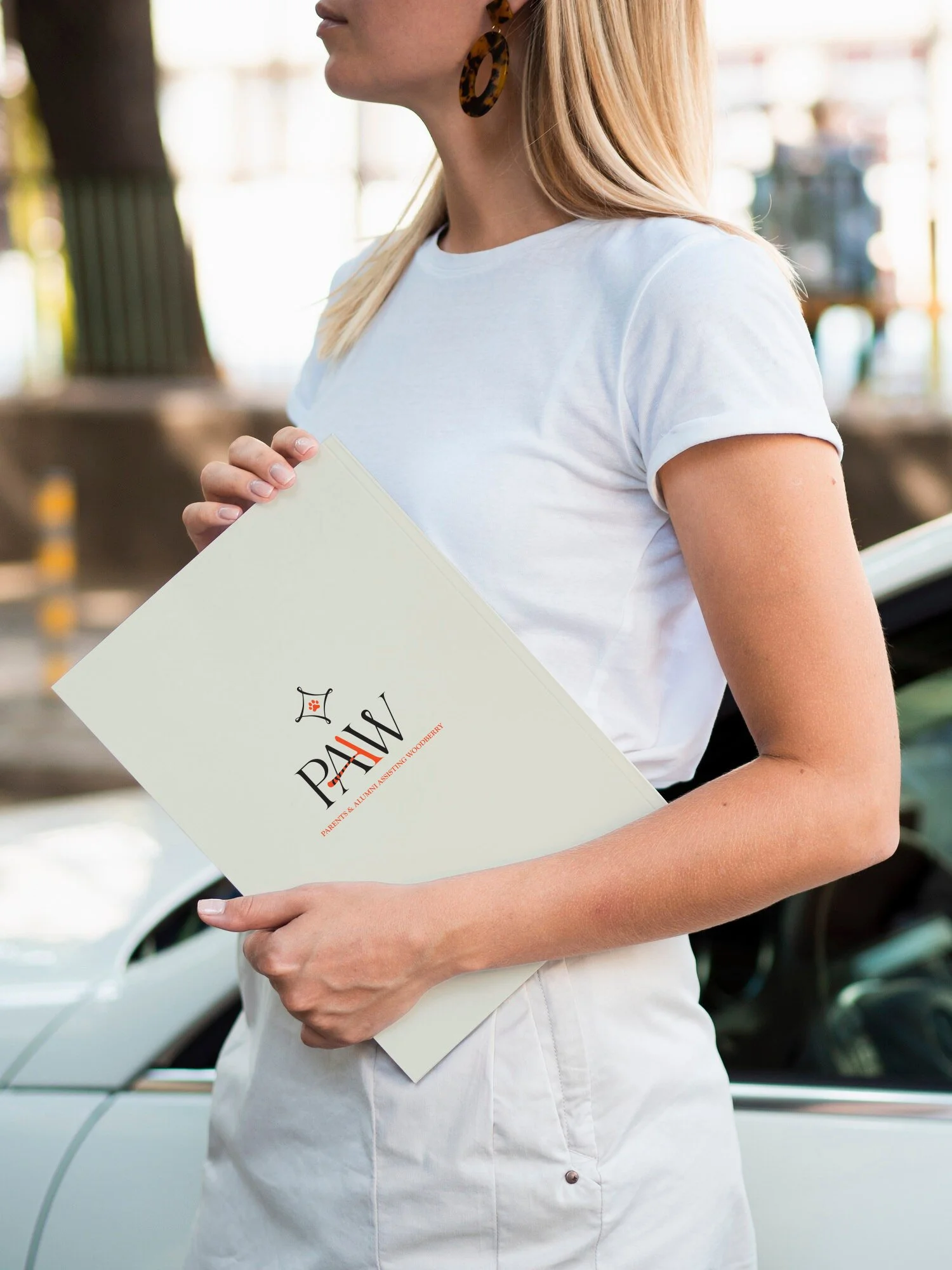 A woman holding a beige folder featuring the PAAW logo designed by Fresh Picked Design for Woodberry Forest School.