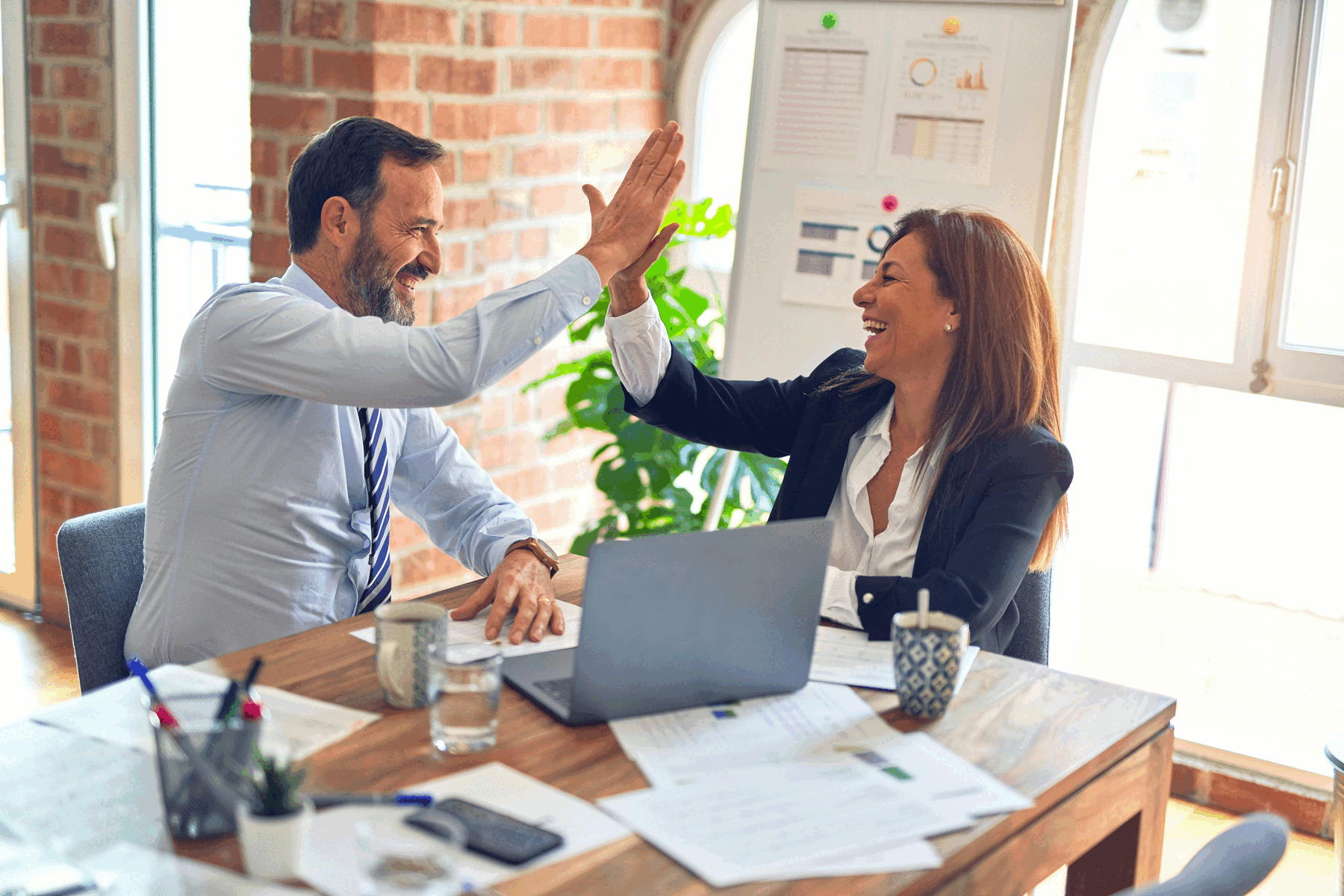 Man and woman in business attire giving each other a high five at a table.