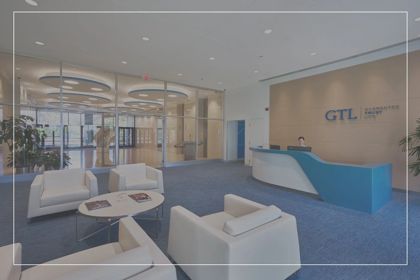 Modern office reception area with blue and white decor, including a reception desk, white seating, glass walls, and a sign reading 'GTL Guarantee Trust Life.'