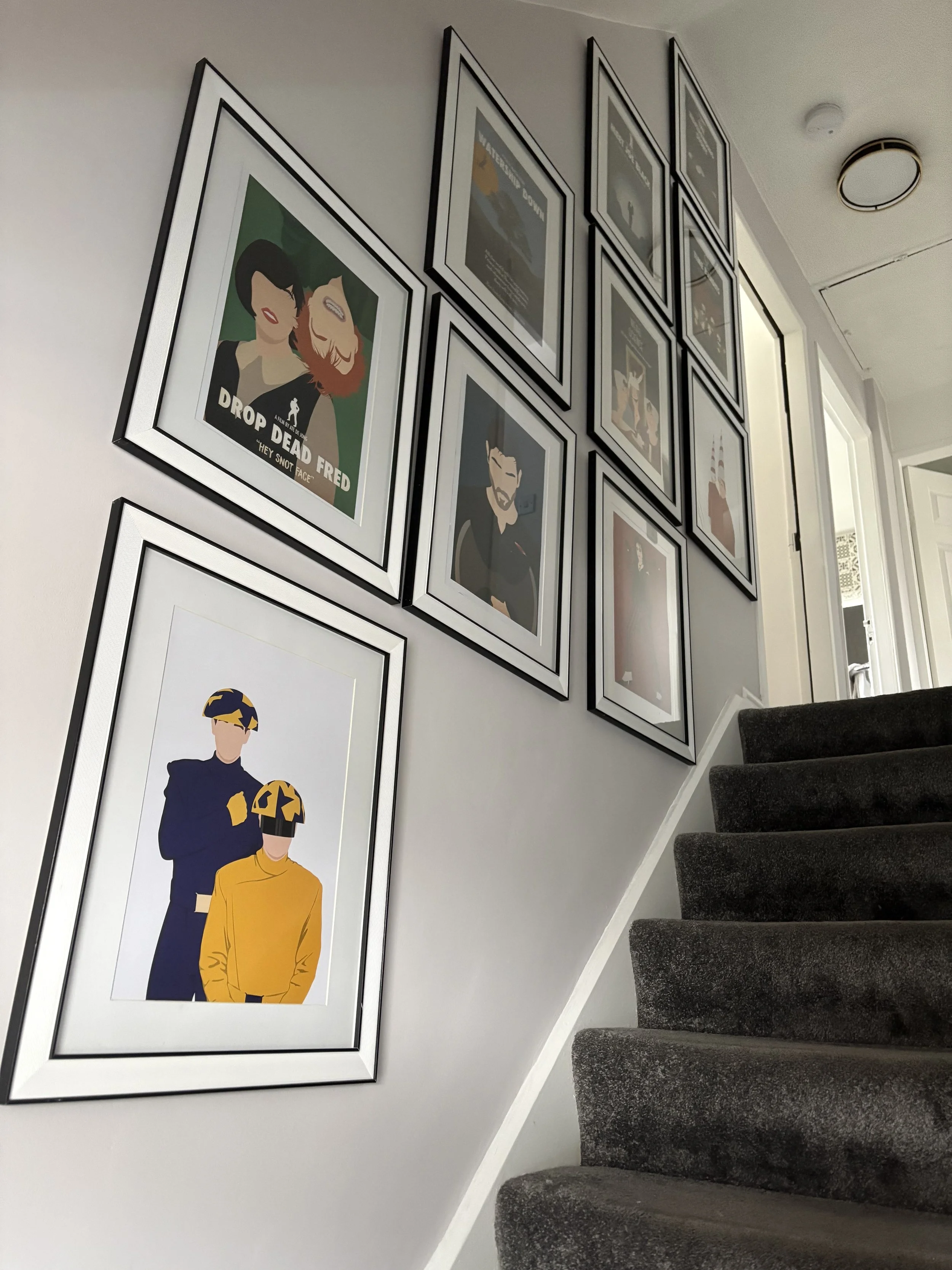 Wall decorated with framed art and posters, next to a dark gray carpeted staircase.