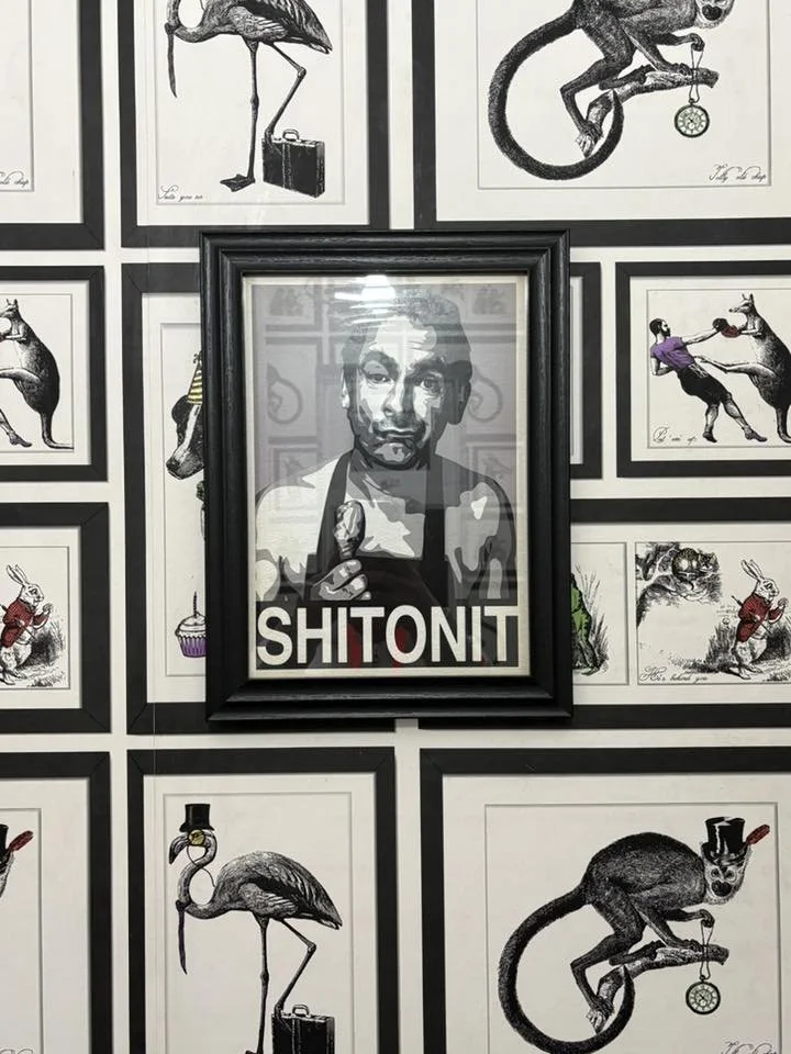 Framed black-and-white portrait of a man holding a phone, with the word 'SHITONIT' below, surrounded by various artistic illustrations of animals, including flamingos wearing hats and monocles, rabbits, and monkeys, in black and white.