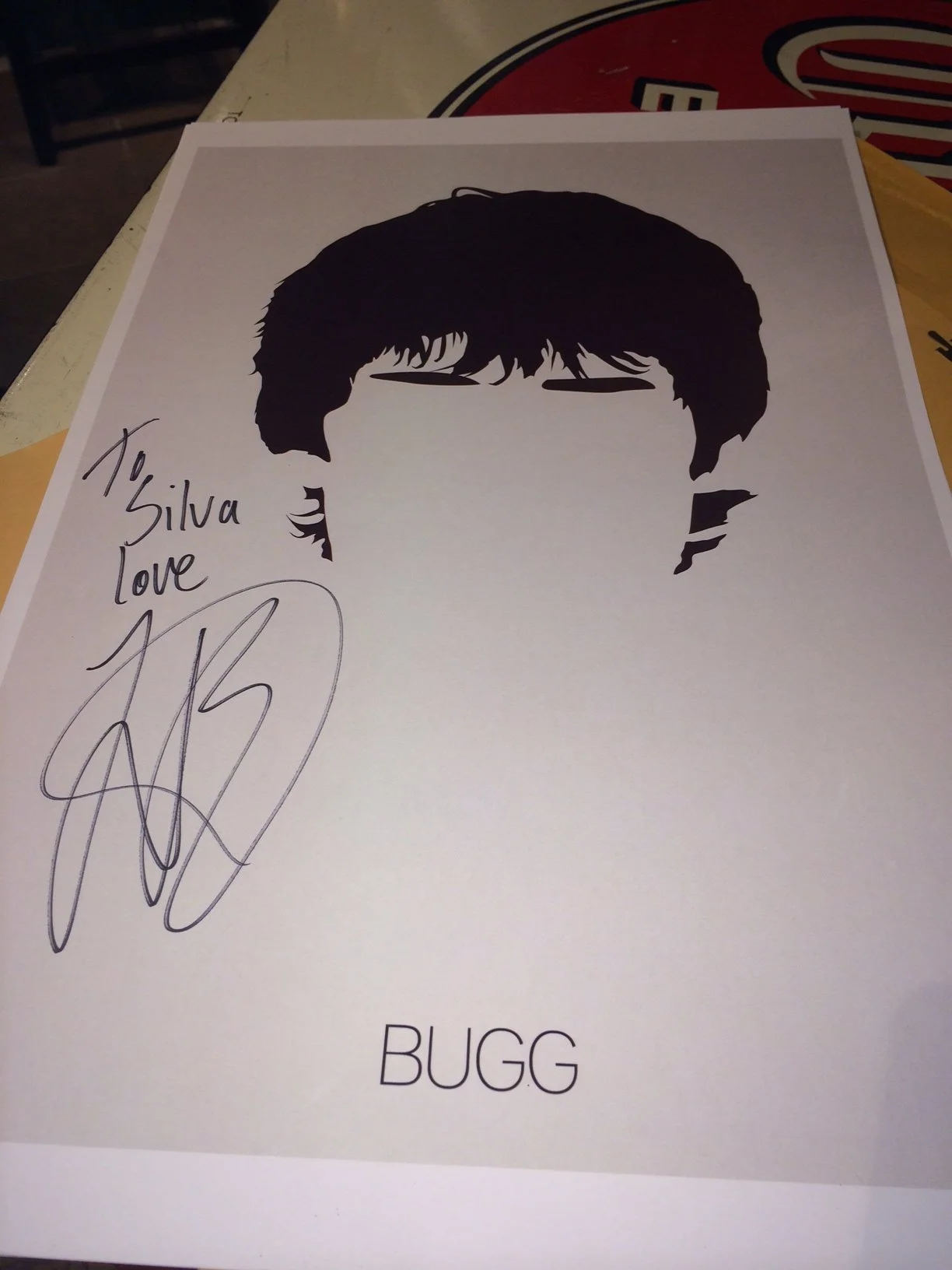 Sign with a silhouette of a person with glasses and dark hair, signed with a message and signature, and the name 'BUGG' at the bottom.