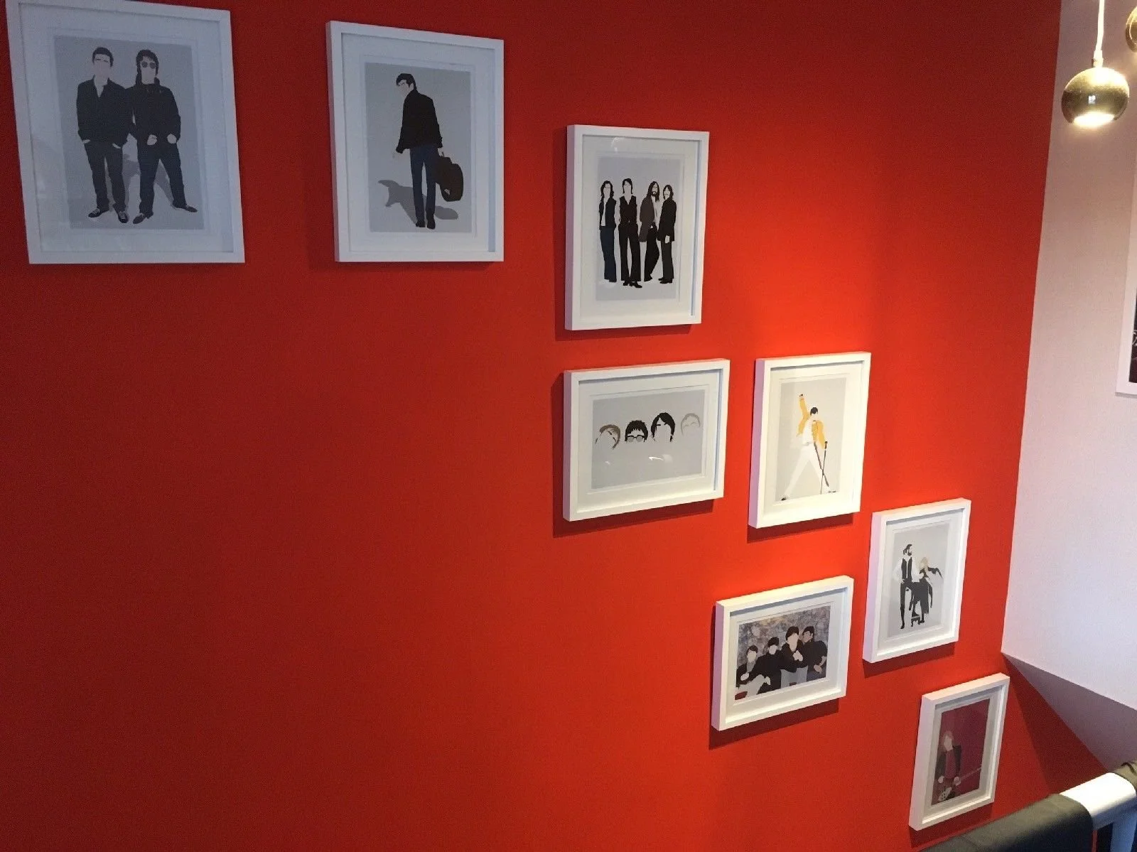 A red wall decorated with framed minimalist art illustrations of various people, some in groups, some alone, some holding objects, in white frames.