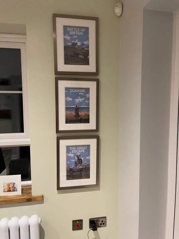 Three framed photographs on a light green wall, titled "Battle of Britain," "Dunkirk," and "The Great Escape," each depicting scenes from World War II evacuation and escape stories.