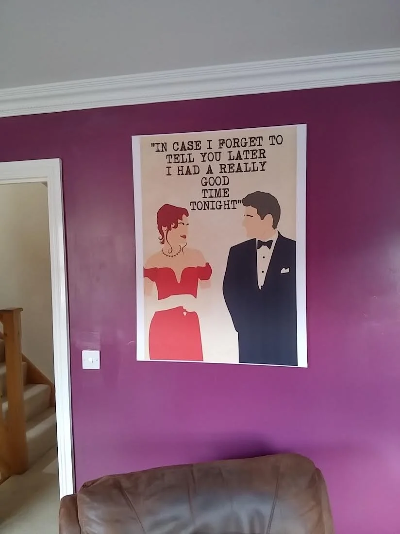 A wall poster features an illustration of a woman in a red dress and a man in a black tuxedo with a bow tie, looking at each other. The poster contains a quote: 'In case I forget to tell you later I had a really good time tonight.' The wall is painte