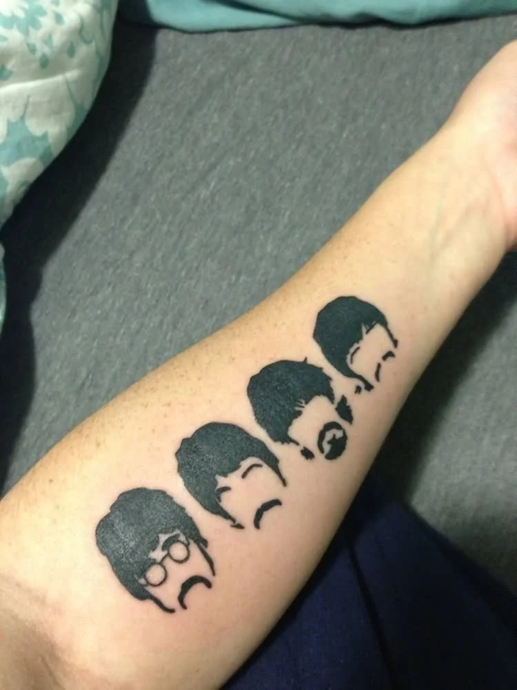 Tattoo of four minimalist black silhouettes of a man's head with different hairstyles and facial hair, arranged in a row on a forearm.