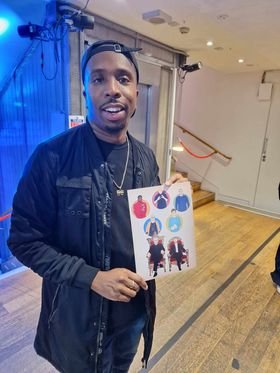 Man holding artwork featuring colorful characters in an indoor gallery or event space.