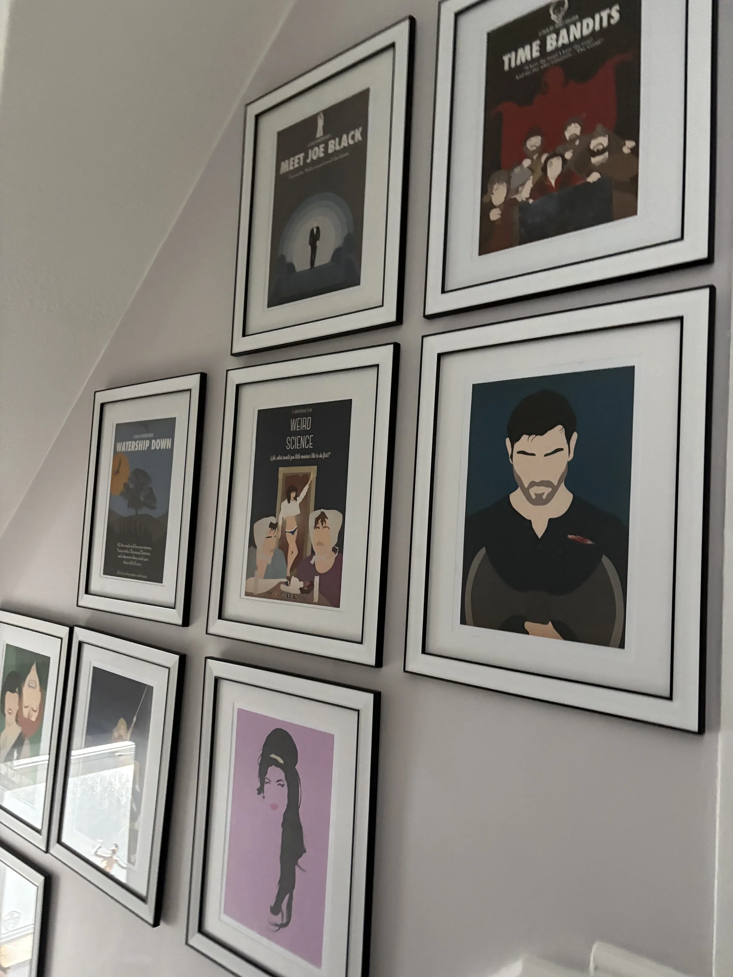 A wall decorated with framed posters of various illustrated portraits and graphic art. The posters include titles like 'MEET JOE BLACK' and 'TIME BANDITS'.