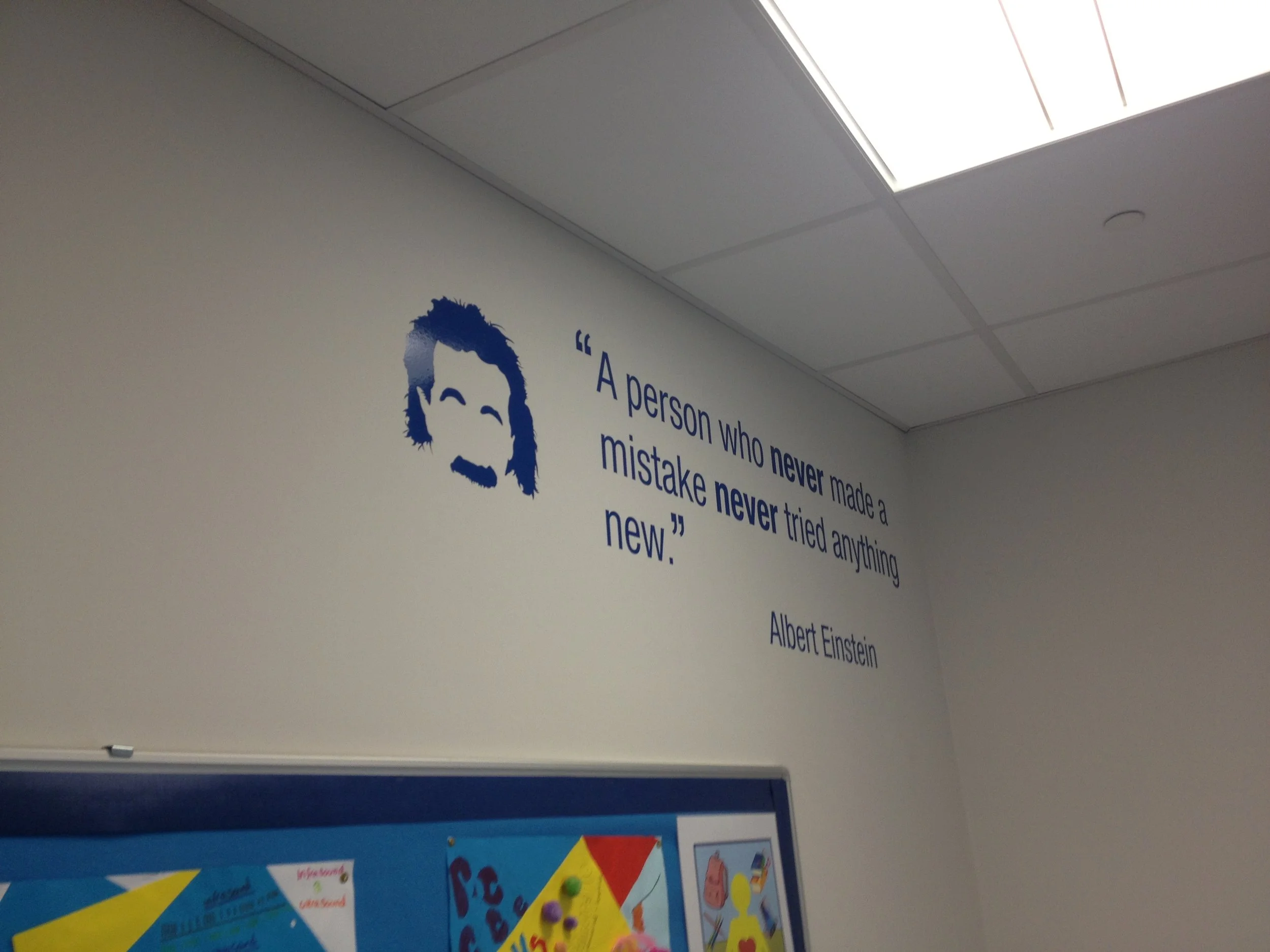 Part of a wall in an educational setting with a quote by Albert Einstein next to a blue illustration of Einstein and part of a colorful bulletin board below.