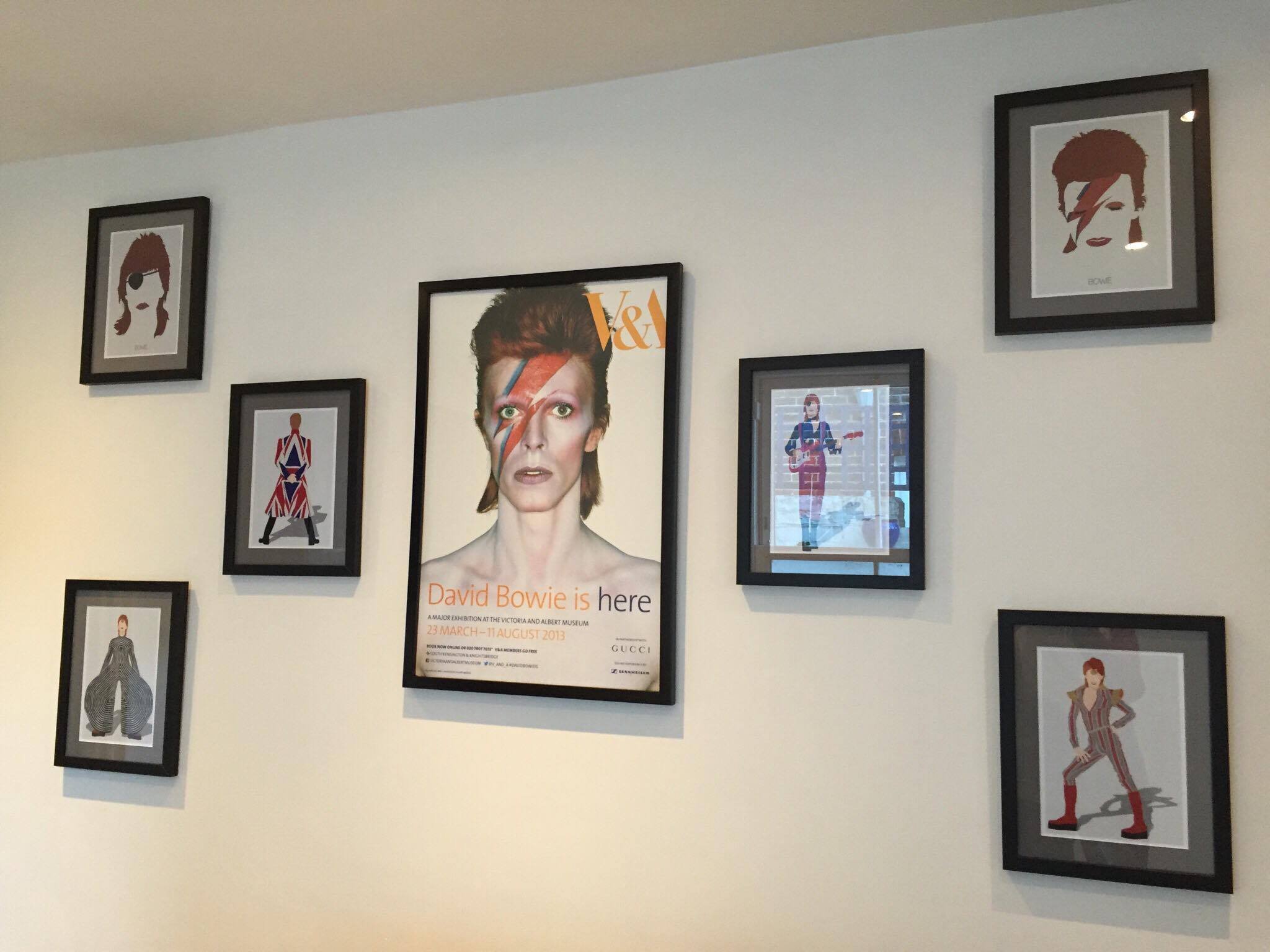 Gallery wall with framed art and a poster of David Bowie with his iconic lightning bolt makeup, and illustrations of various fashion figures.