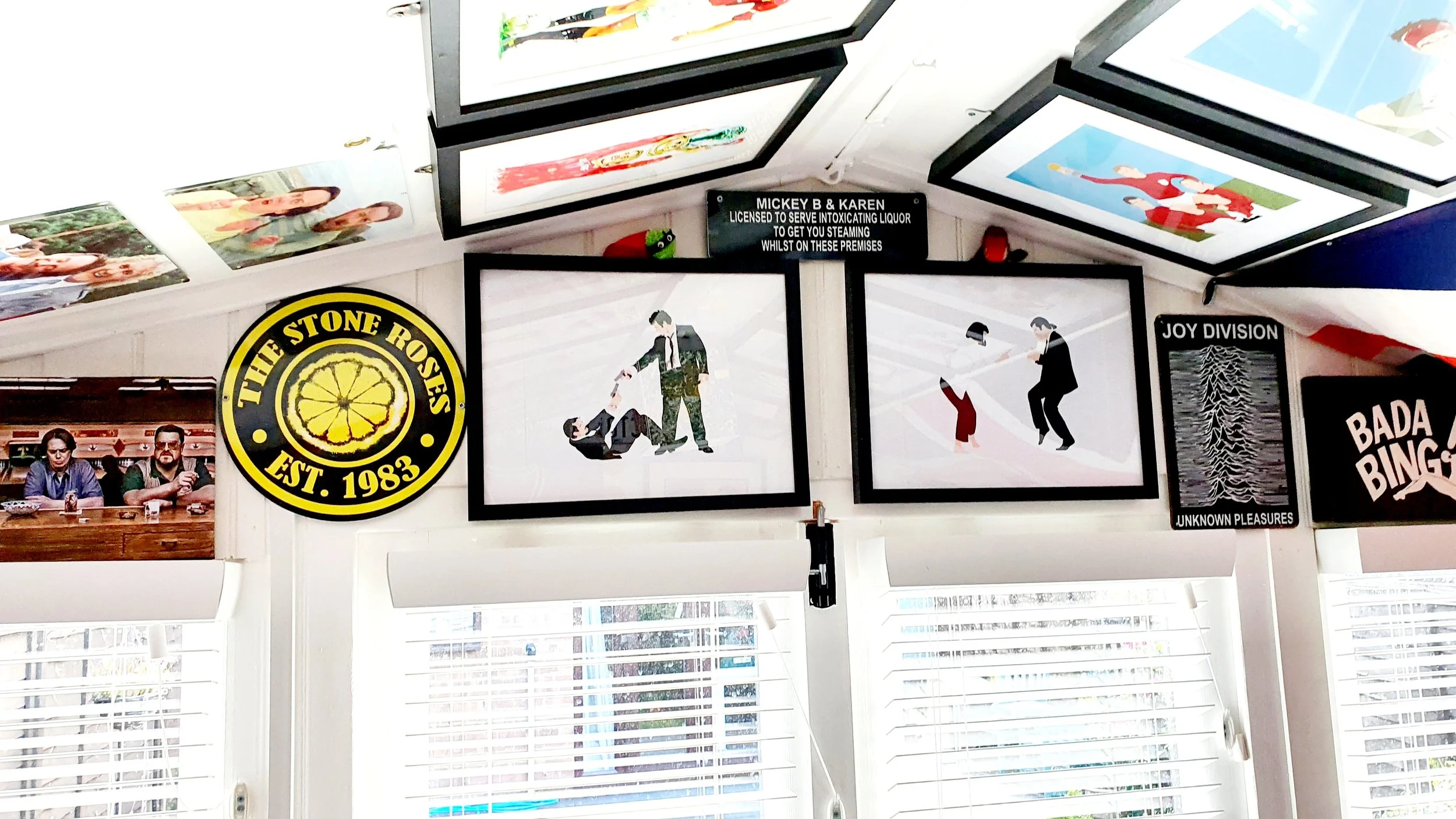 Decorative wall with framed artwork, signs, and photographs, including a logo for The Stone Rose established in 1983, and illustrations of people, including one performing a humorous dance, and a man waiting with a woman. The ceiling displays various
