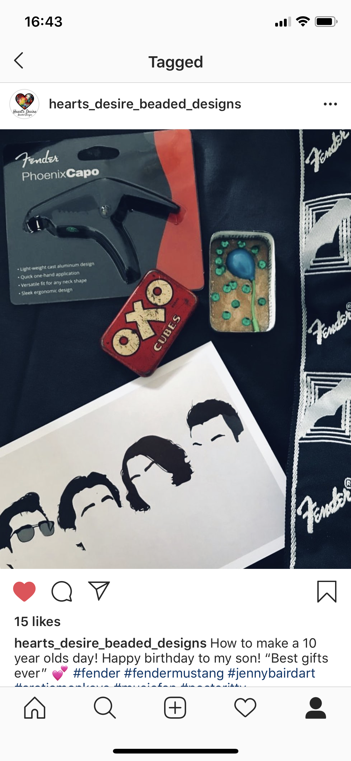 Collection of items including a guitar pick holder labeled 'Fender Phoenix Capo,' a red box of 'OXO Cubes,' a small tray with a mini blue balloon and green beads, a drawing of four stylized faces, and a black cloth with 'Fender' logos.