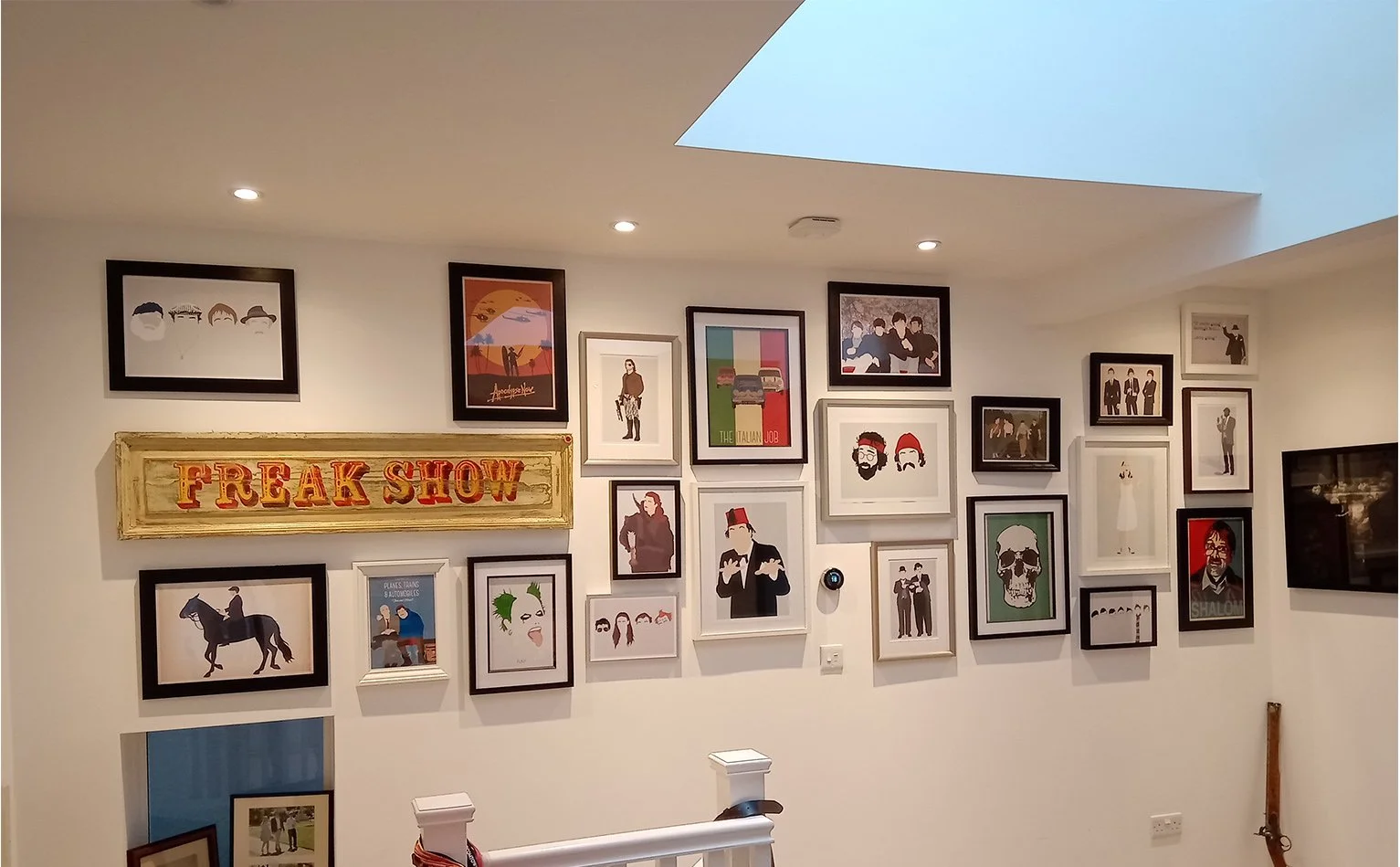 A gallery wall with various framed art and photographs, including a sign that reads "FREAK SHOW" in vintage style lettering, and a skylight in the ceiling.