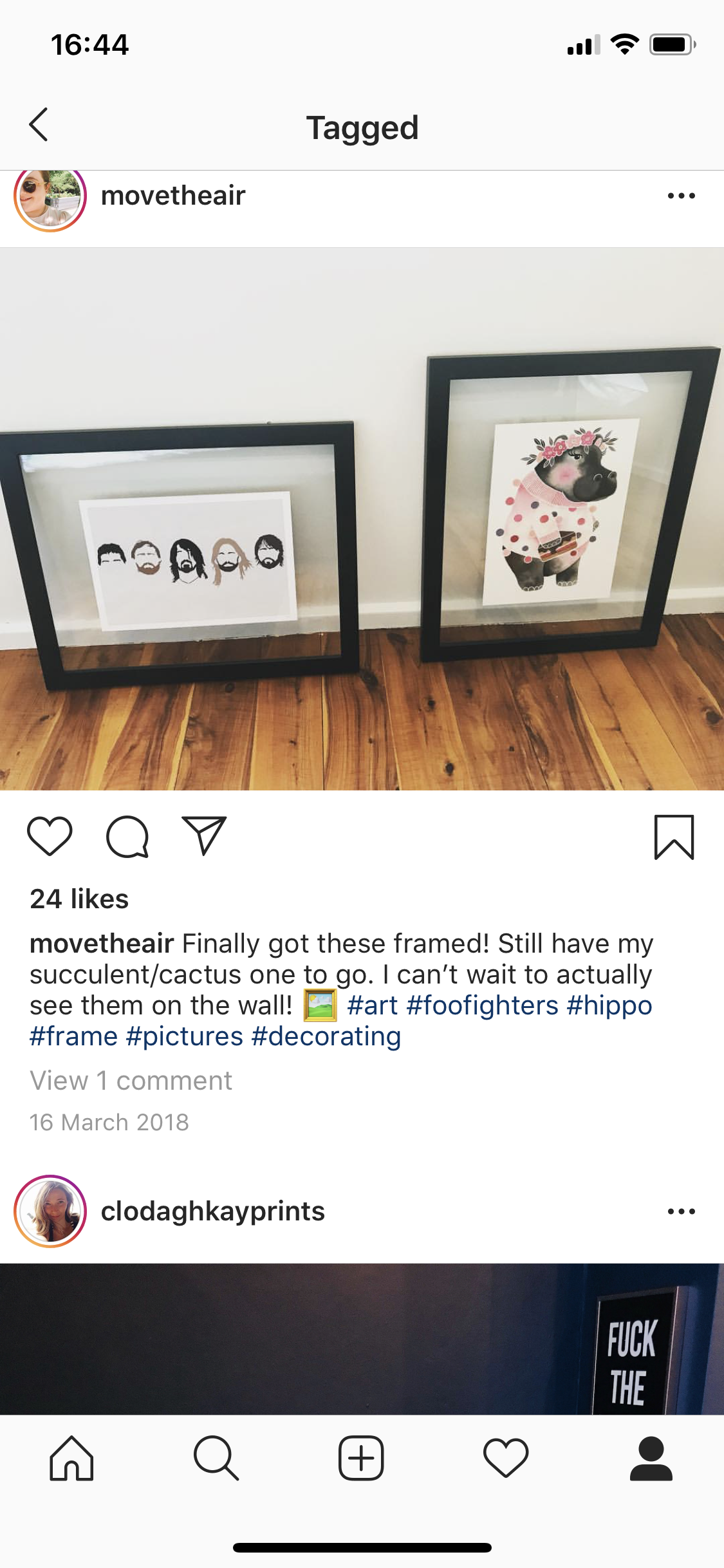Two framed art prints leaning against a white wall on a wooden floor. The left print is a minimalist black-and-white illustration of five people with different hairstyles and facial hair, and the right print is a cute, stylized drawing of a hippo wea