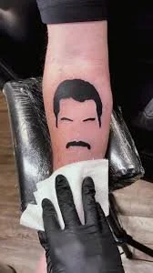 Tattoo of a face with a beard and hat being cleaned with a cloth.